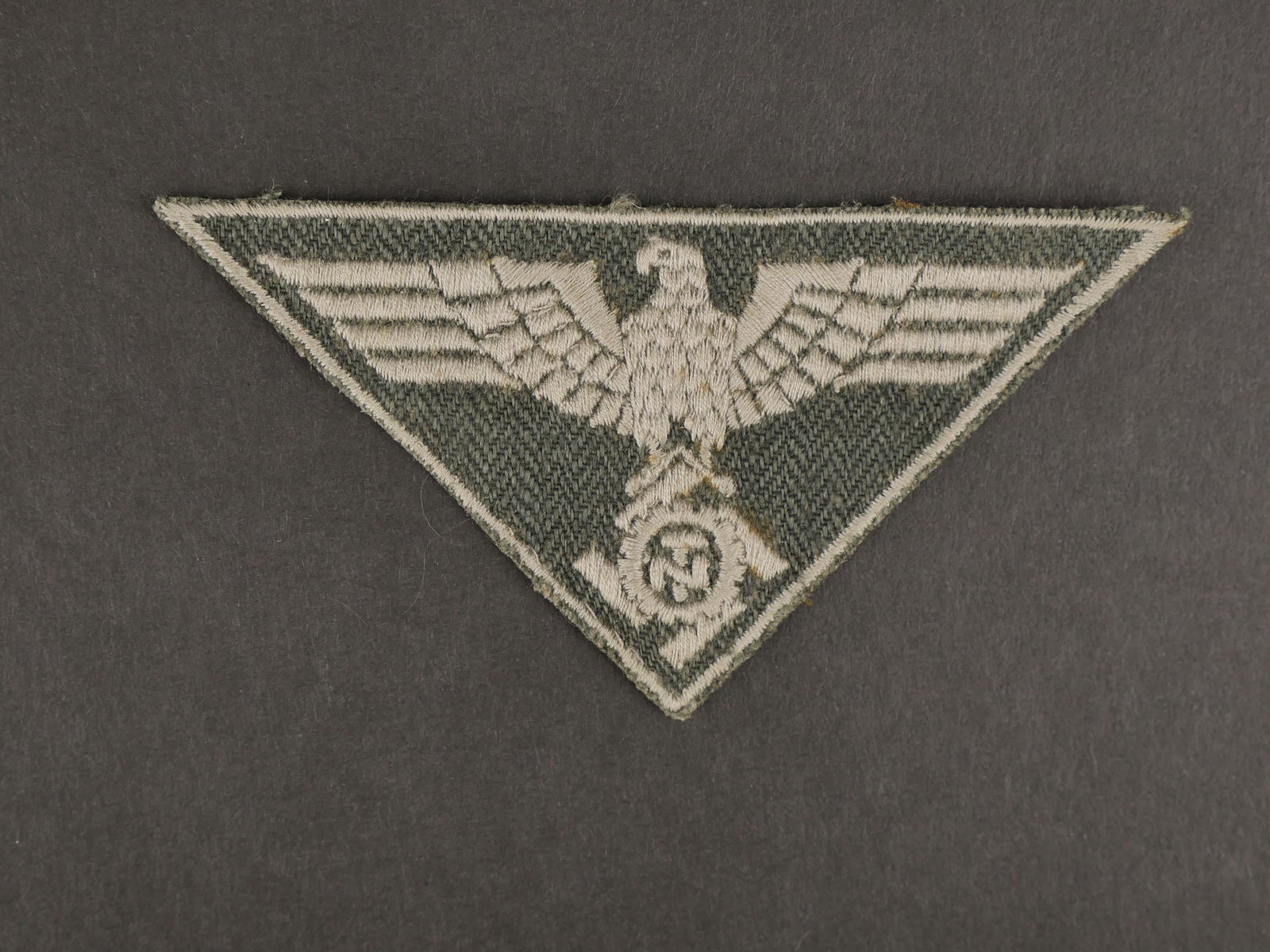 Aigle de poitrine du Teno. Teno s breast eagle.: Aigle de poitrine du Teno. Modele brode en fils gris clair sur fond gris. Insigne triangulaire. Visiblement jamais monte. Traces de colle au dos. A noter une certaine usure et patine de la piece. Etat