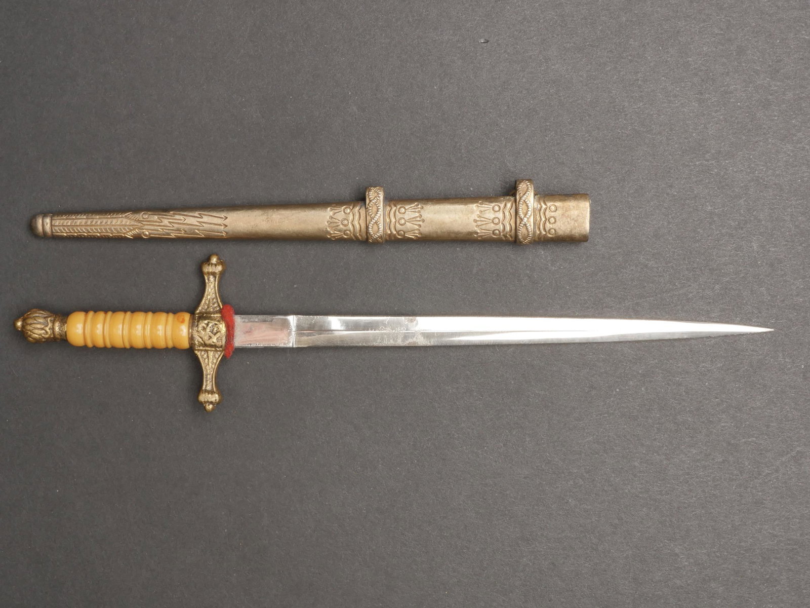 Miniature de dague Reichsmarine. Reichsmarine dagger miniature.: Miniature de dague Reichsmarine. Toutes les garnitures sont en metal dores. Les details sont tres difficilement distinguable. Poigne legerement tordue. Manche de couleur orange. Fourreau grave d eclai