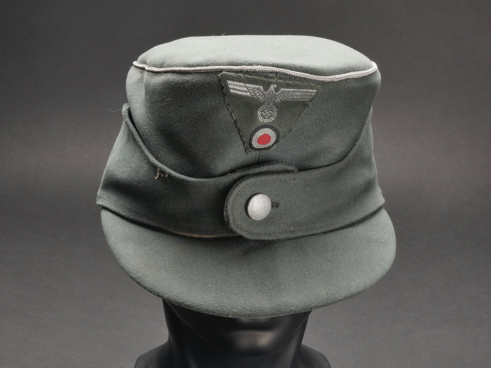Casquette M-43 officier Heer. German M-43 officer cap.: Casquette M-43 d officier de la Heer. En gabardine Feldgrau. Lisere argent faisant le tour de la coiffure. Insigne tisse trapezoidal, monte main. Un bouton grenele pour le maintien du rabat. Interieur