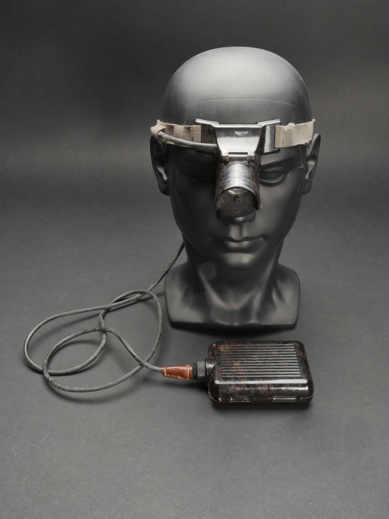 Lampe frontale. Headlamp.: Lampe frontale pour casque allemand. Lampe en bakelite, ampoule presente, toutes les pieces mobiles sont fonctionnelles. Sangle de fixation complete, avec son crochet de fermeture. Elastique sec et ca