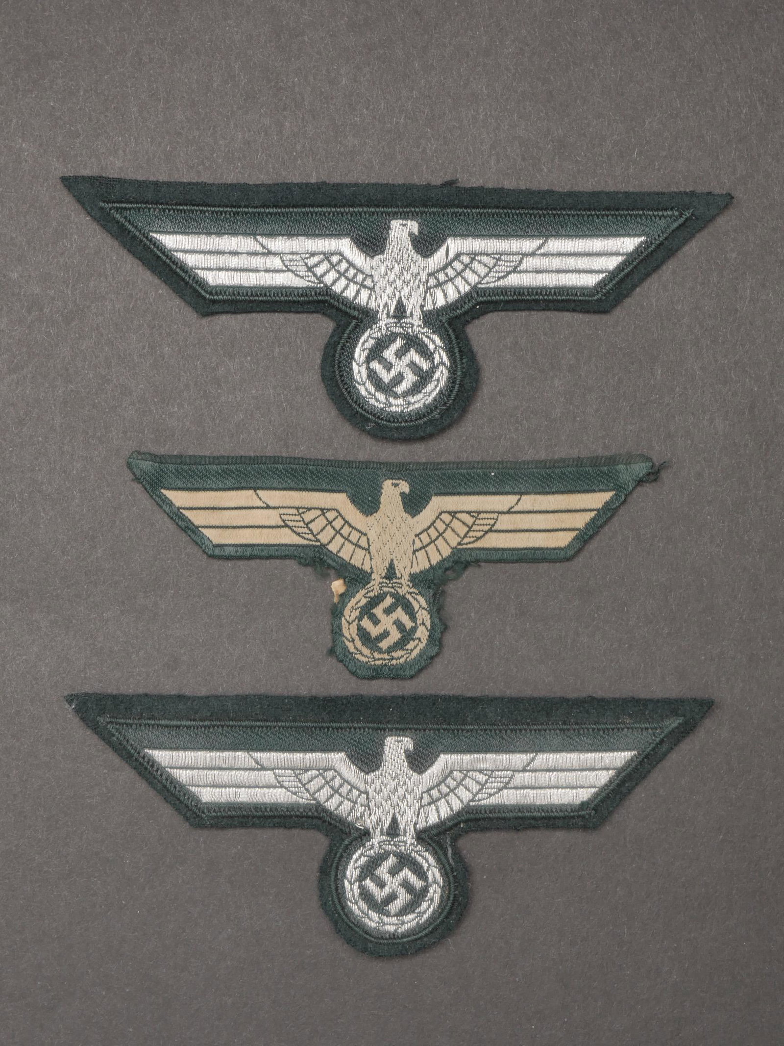 Aigles de poitrine Heer. Heer chest eagles.: Aigles de poitrine Heer. Comprenant un aigle de poitrine Bevo, visiblement demonte d une vareuse, traces de colle au dos. Un aigle de poitrine tisse sur fond en drap vert canard, jamais monte, format 
