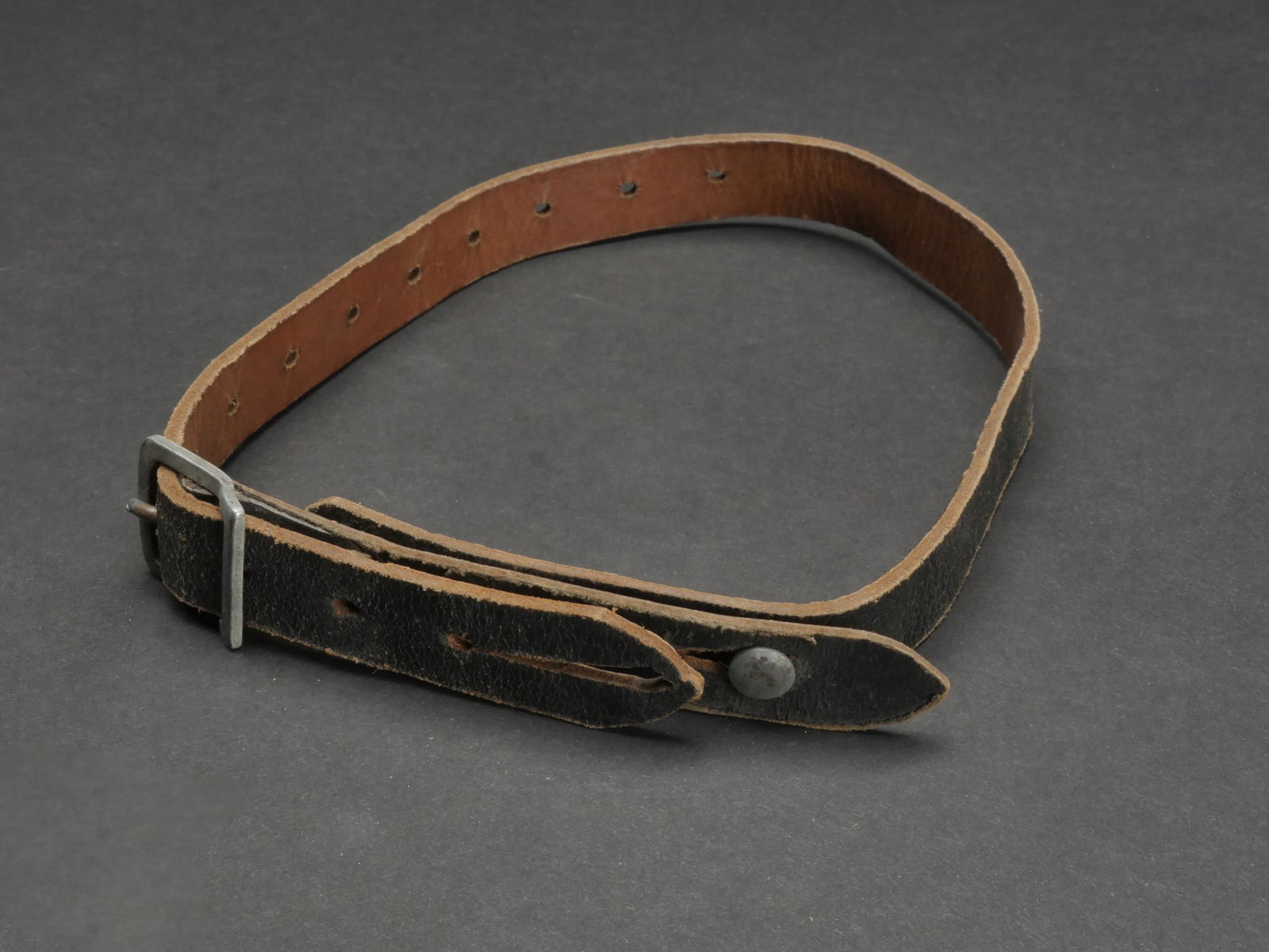 Jugulaire de casque. Helmet chinstraps: Jugulaire de casque allemand. En cuir. Les tetons en metal sont presents. Boucle a ardillons complete. Treize trous de reglage. Sans marquages visibles. A noter une certaine usure et patine de la piec