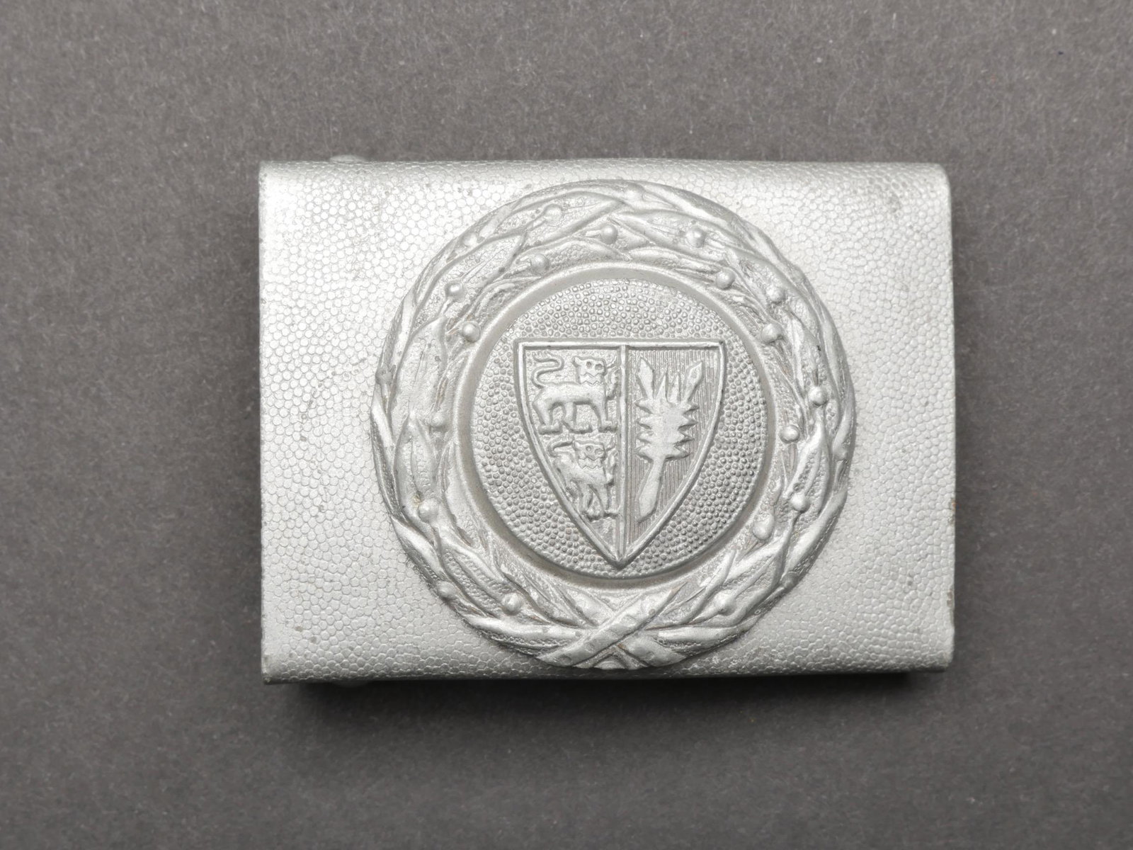 Boucle de ceinturon du Schleswig Holstein. Schleswig Holstein Belt buckle.: Boucle de ceinturon du Schleswig Holstein. En aluminium grenele. Fabrication en deux parties. Boucle a deux ardillons complete. Sans marquages visibles. A noter une certaine usure et patine de la piec