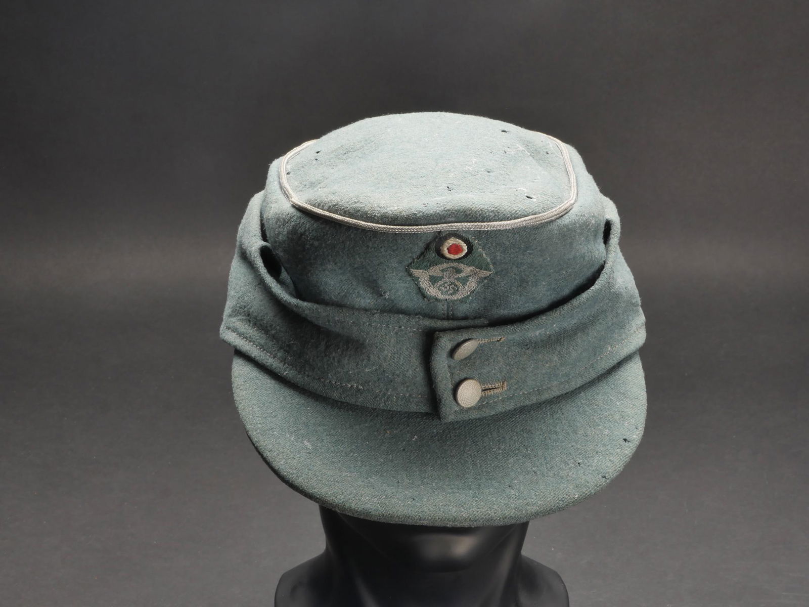 Casquette officier Polizei. Polizei officer cap.: Casquette d officier Polizei. En drap gris/vert. Lisere argent faisant le tour de la coiffure. Deux boutons greneles fermant les rabats. Insigne polizei tisse, montage manuel. Interieur double en tiss