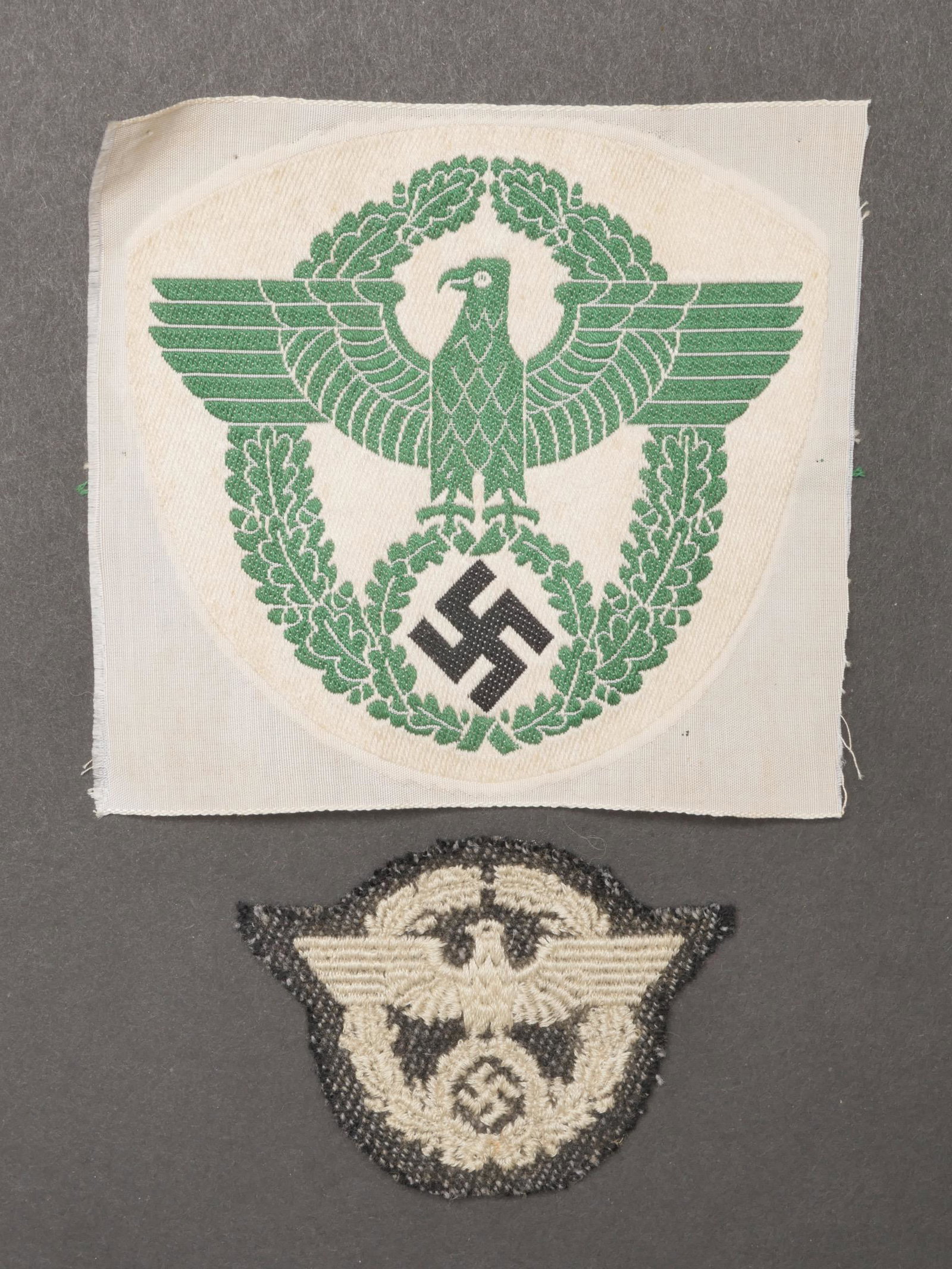 Insignes Polizei. Police insignia.: Insignes Polizei. Comprenant un insigne de maillot de sport tisse sur fond blanc, jamais monte. Un insigne de coiffure Polizei brode blanc, sur fond gris/bleu. A noter une certaine usure et patine des