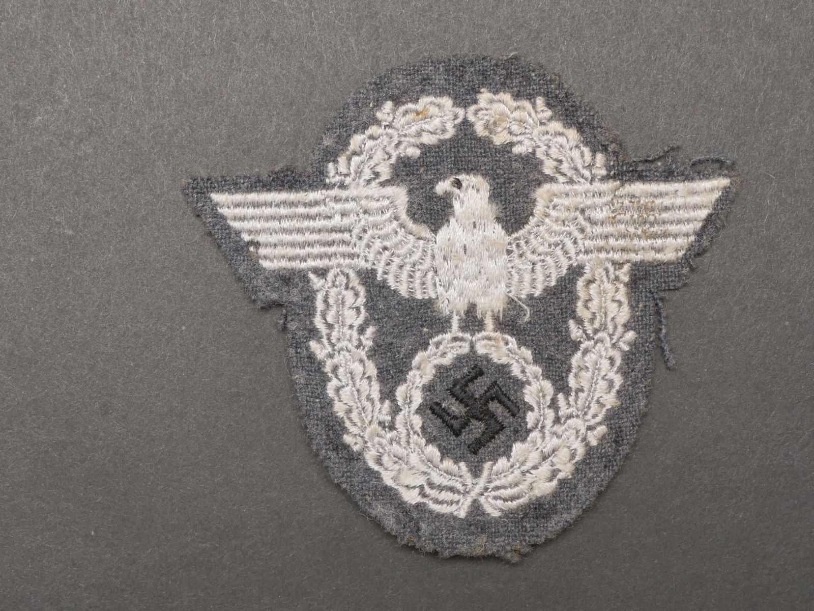 Insigne Schutze Polizei. Schutze Polizei insignia.: Insigne Schutze Polizei. Modele pour sous-officier brode sur fond gris. Traces de colle au dos. A noter une certaine usure et patine de la piece. Etat II+. Badge Schutze Polizei. Model for non-commiss
