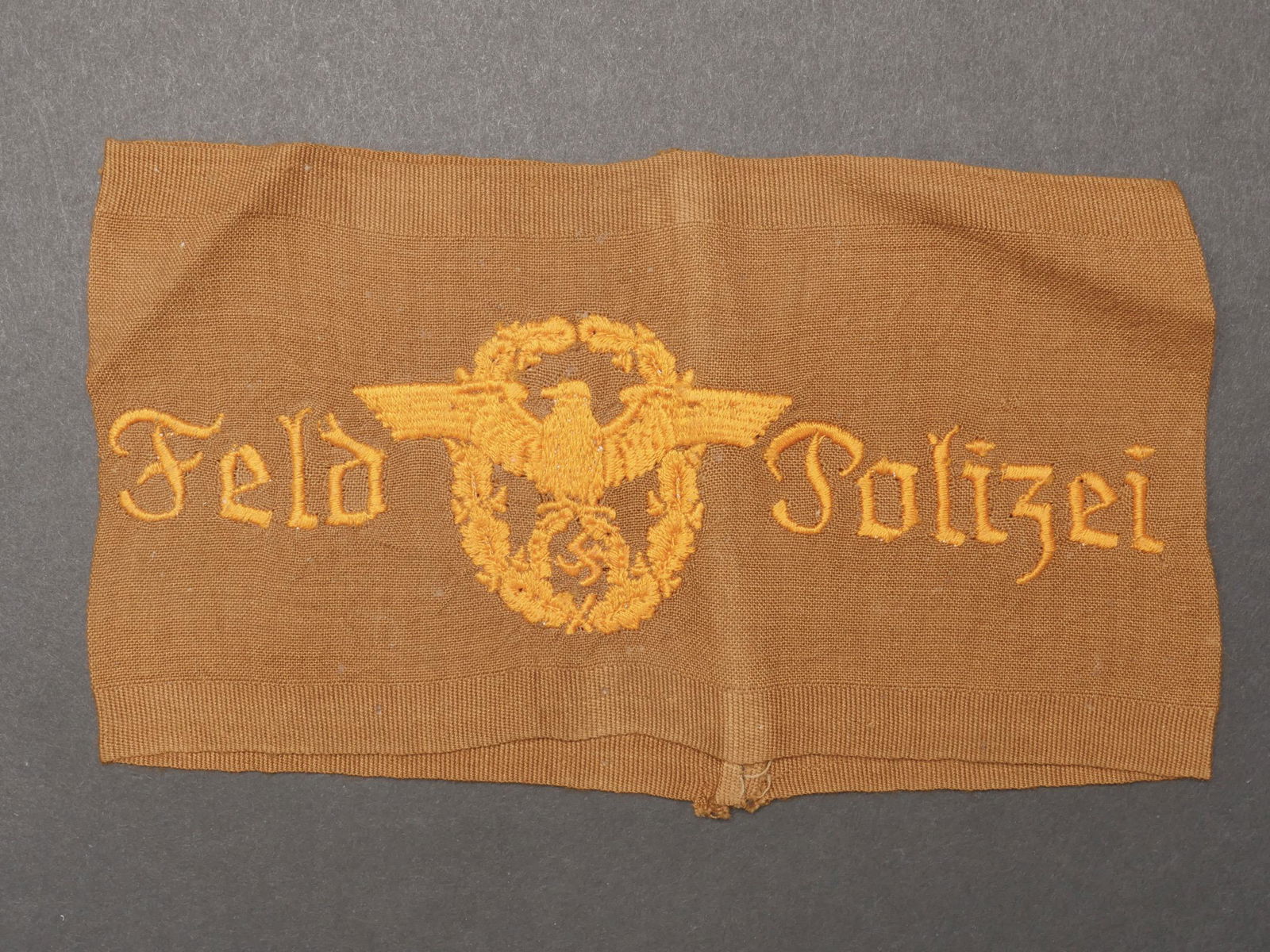 Brassard Feld Polizei. Feld polizei armband.: Brassard Feldpolizei. En tissu coton marron. Mention Feld Polizei et insigne Polizei brodes. Sans marquages visible. A noter une certaine usure et patine de la piece, ainsi que quelques t aches. Etat