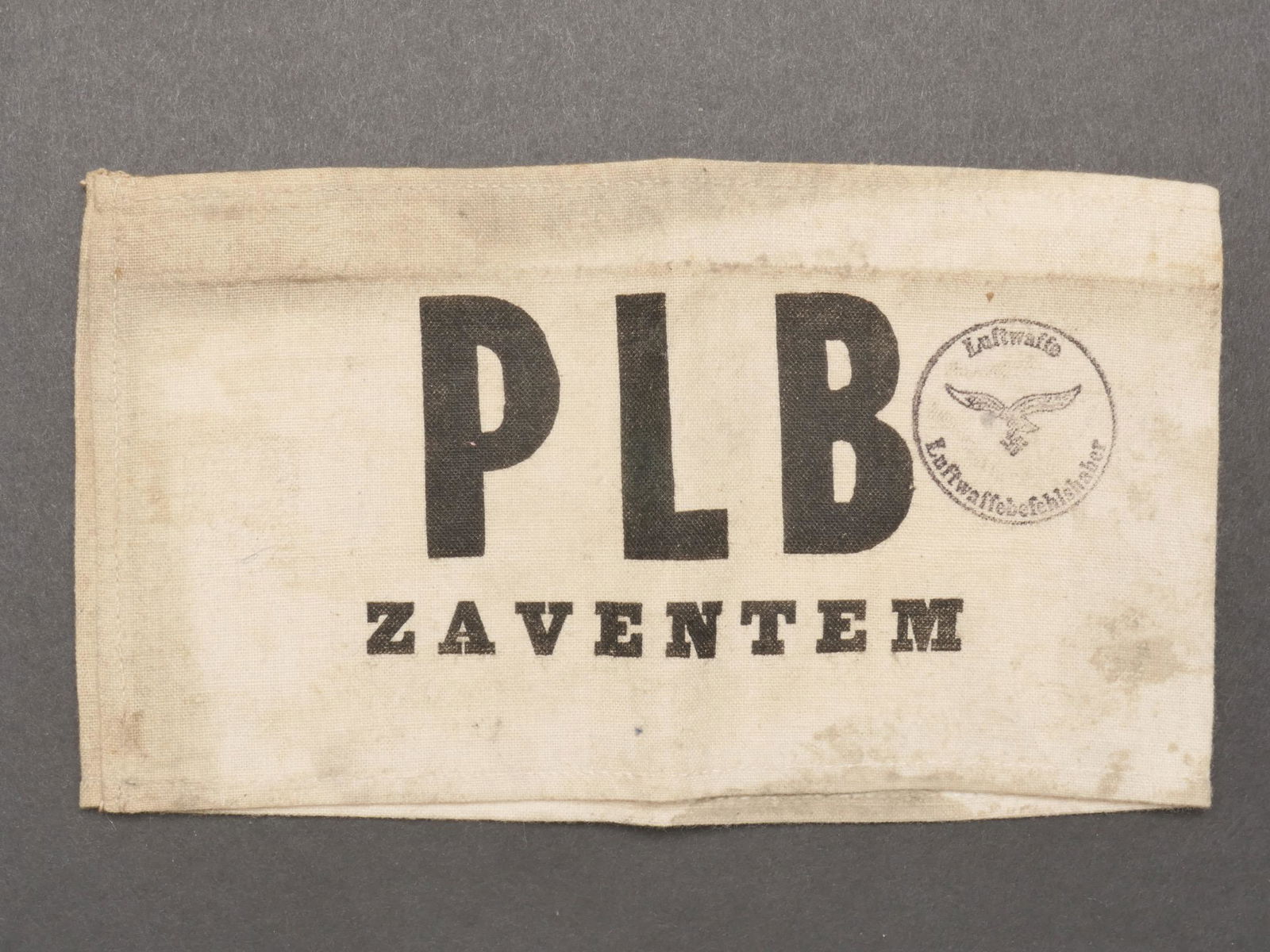 Brassard PBL Zaventem. PBL Zaventem armband.: Brassard d ouvrier travaillant a l aeroport de Zaventen. En tissu coton gris. Marquage imprime PLB Zaventem. Tampon marque Luftwaffe Luftwaffebefehlshaber. Sans marquage fabricant visible. A noter une