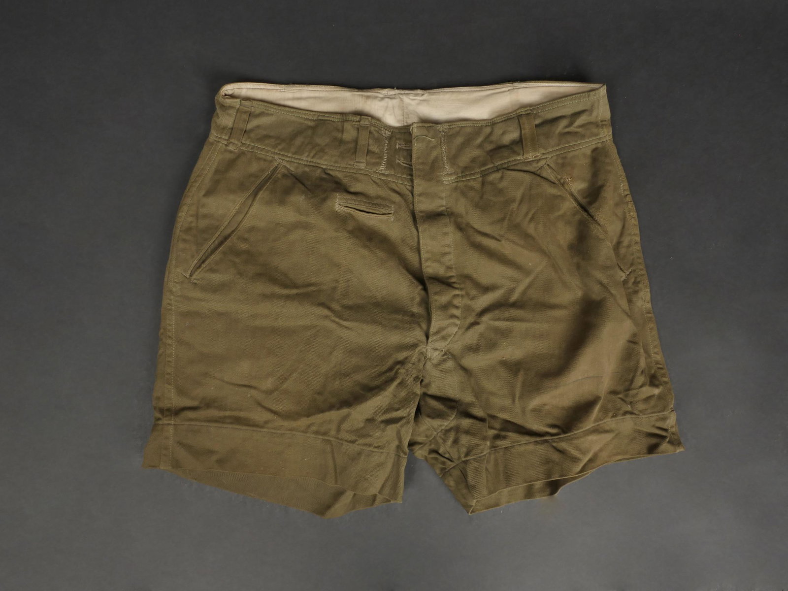 Short tropical. Tropical shorts.: Short tropical. En toile vert kaki. La majorite des boutons sont presents. La ceinture de serrage est absente, les orifices ont ete cousus. Interieur double en tissu coton blanc. Marquages RBNr 0/0721