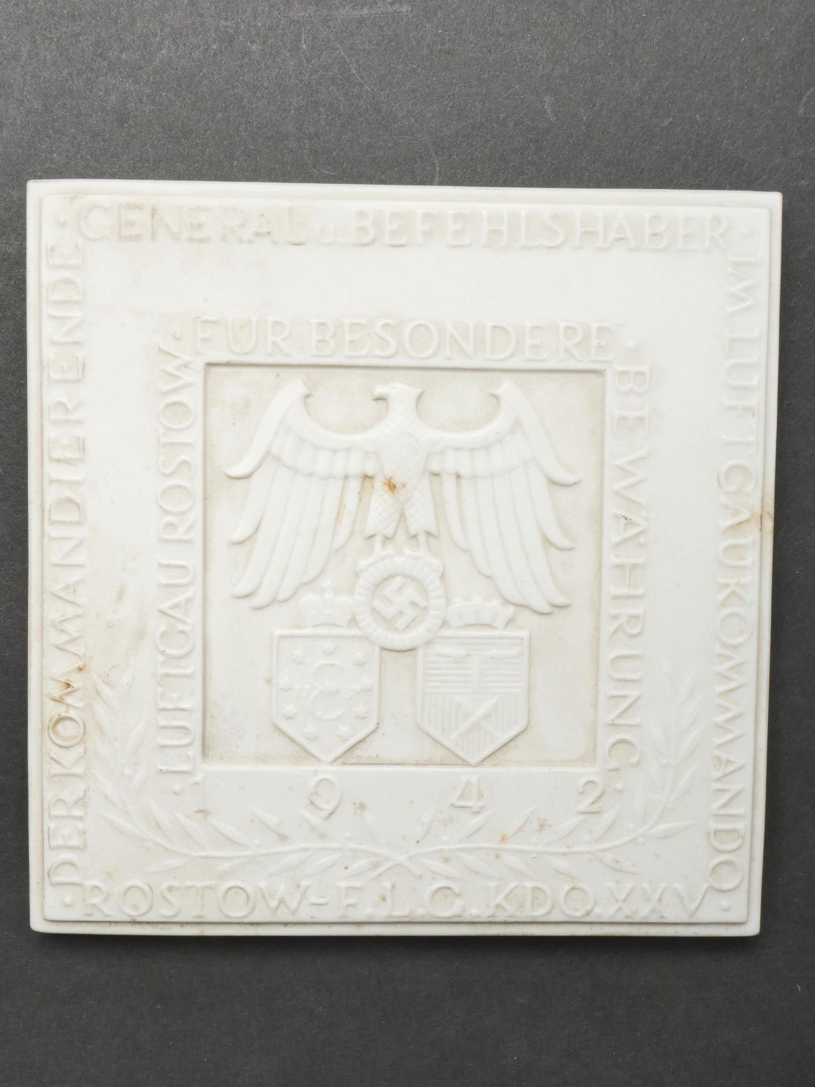 Carreau en faience LW. LW earthenware tile.: Carreau en porcelaine Luftwaffe. En porcelaine blanche, mentions et decors en relief. Recto bien marque Der Kommandierende General u Befehlshaber im LuftgauKommando Rostow FLG KDO XXV. Au verso marqua