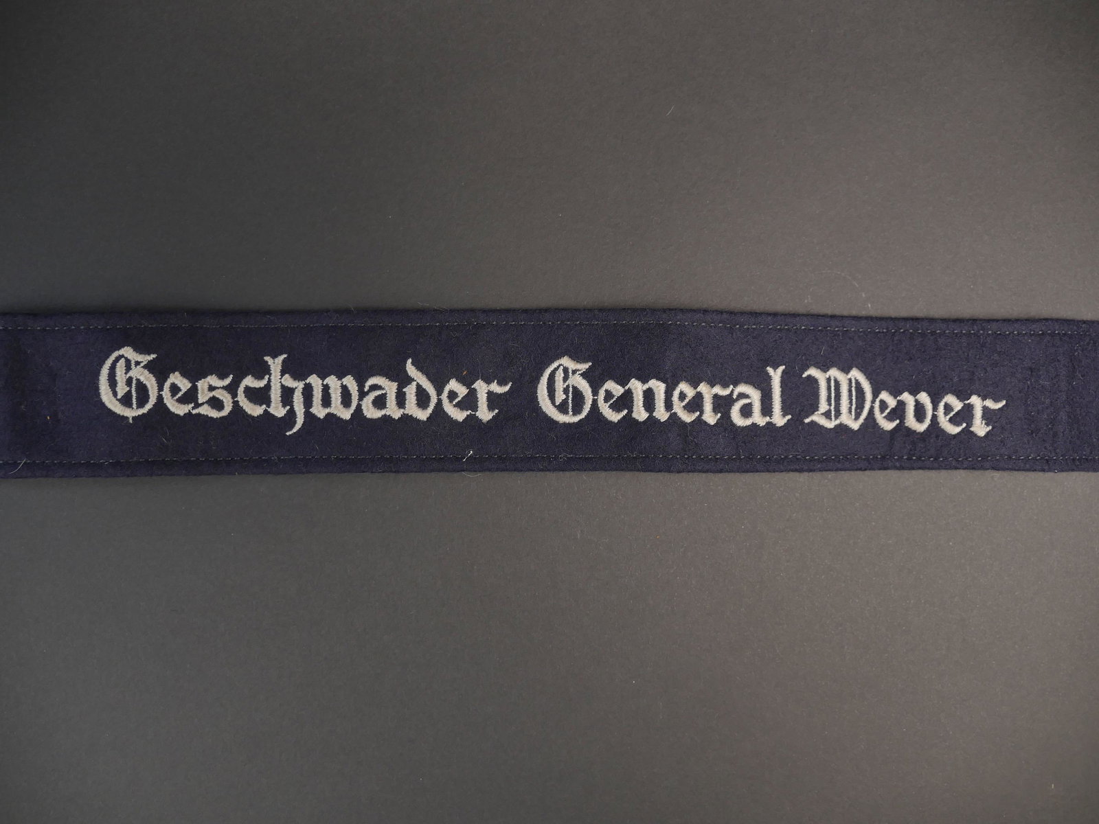 Bande de bras LW. Luftwaffe cufftittle.: Bande de bras Geschwader General Wever. En drap gris/bleu. Marquage brode Geschwader General Wever. T aches au dos de la piece. Dimensions 4 x 44 cm. A noter une certaine usure et patine de la piece. 
