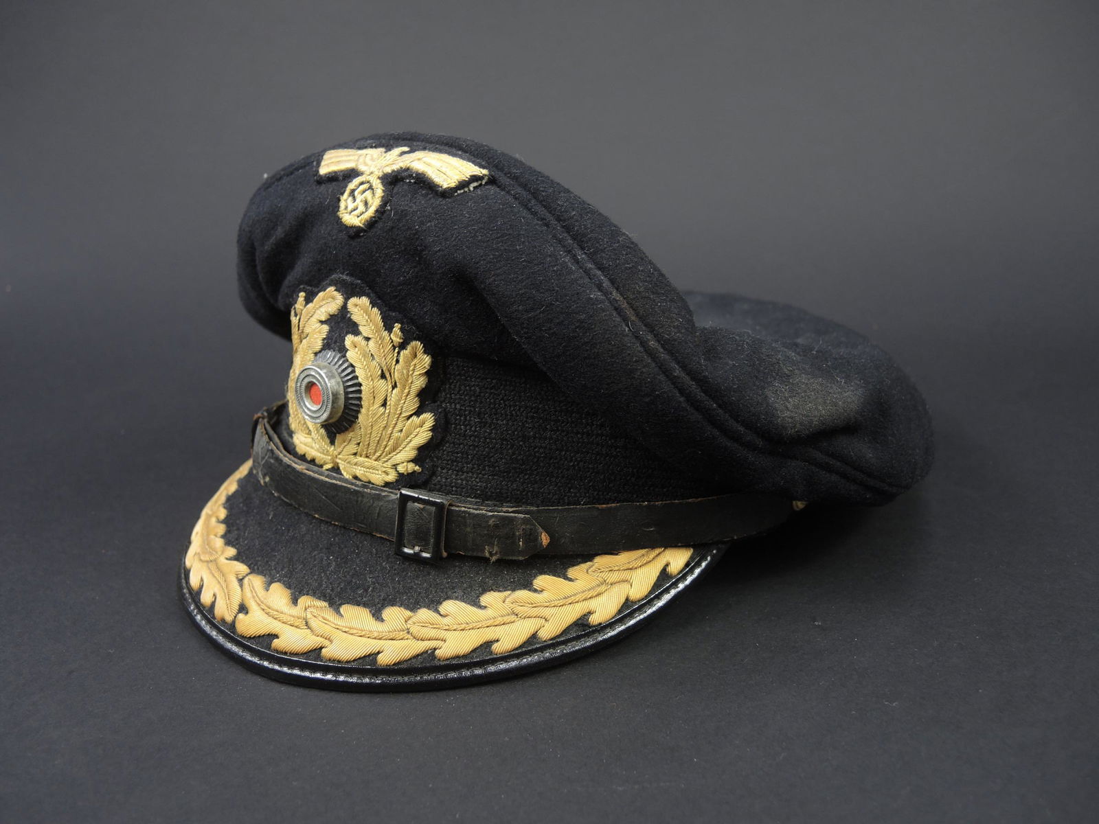 Casquette Kriegsmarine. Kriegsmarine cap.: Casquette Kriegsmarine. Modele pour officier superieur. En drap noir. Visiere recouverte de drap noir, rangee de feuilles de chene doree. Aigle et cocarde brodes. Cocarde metallique. Fausse jugulaire
