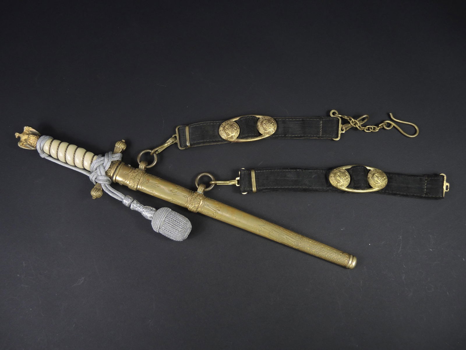 Dague Kriegsmarine. Kriegsmarine dagger.: Dague d officier Kriegsmarine. Garniture en metal dore. Poignee de couleur blanche, filigrane complet. Dragonne nouee de maniere reglementaire. Belieres completes. Fourreau grave d eclairs et presenta