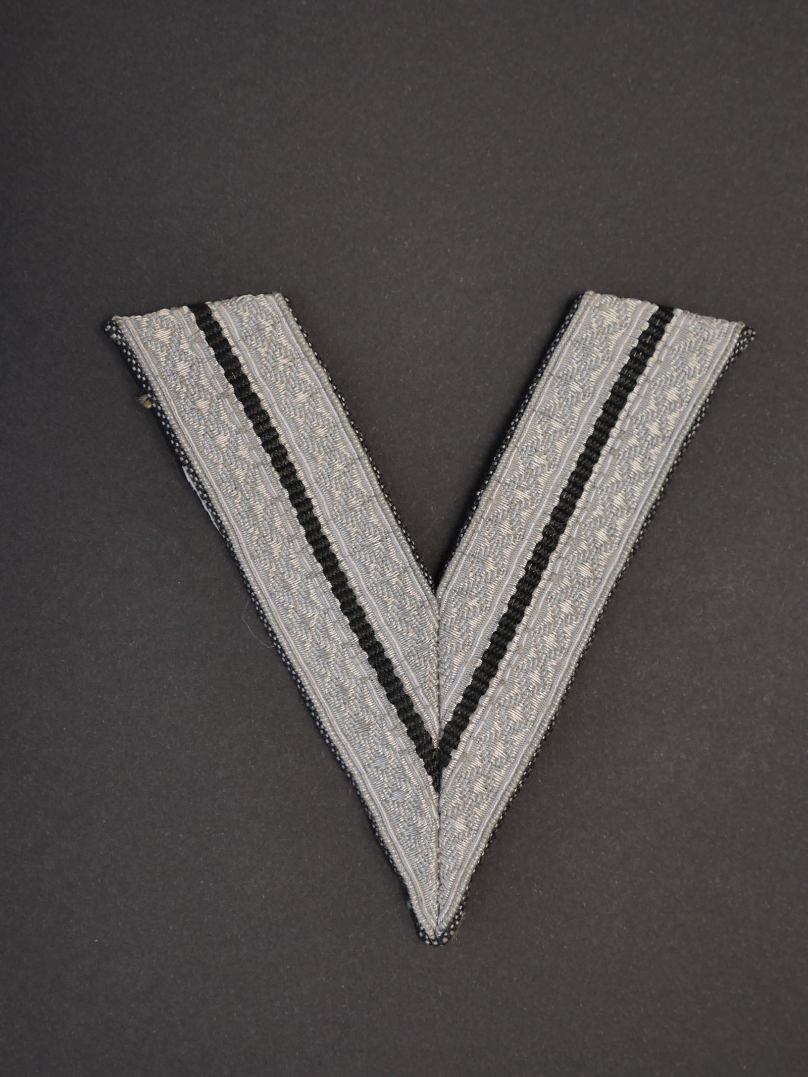 Chevron de grade SS. SS Sleeves rank.: Chevron de grade SS. Couleur argent. Grade de Rottenfuhrer. Traces de colle au dos. A noter une certaine usure et patine de la piece. Etat II+. SS grade chevron. Silver color. Rottenfuhrer grade. Trac