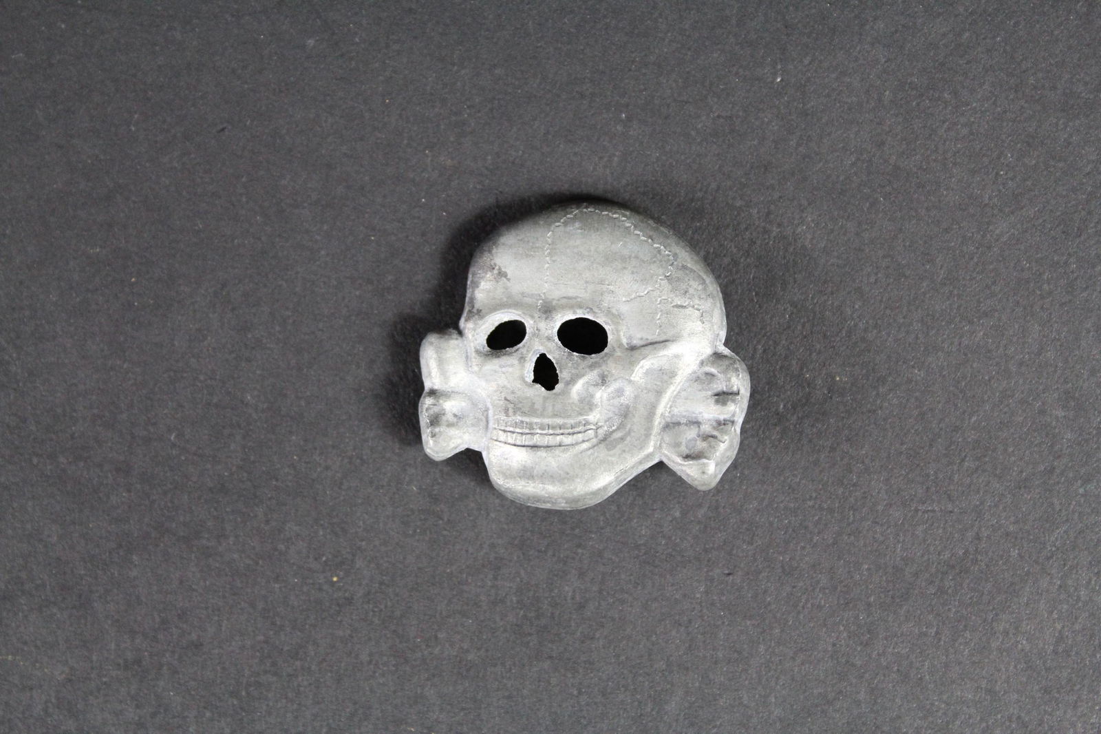 Tete de mort SS. SS skull.: Tete de mort pour casquette SS. En metal. Fabrication en creux. Une attache cassee au dos. Fabrication RZM SS partiellement illisible. A noter une certaine usure et patine de la piece. Etat II+. Skull