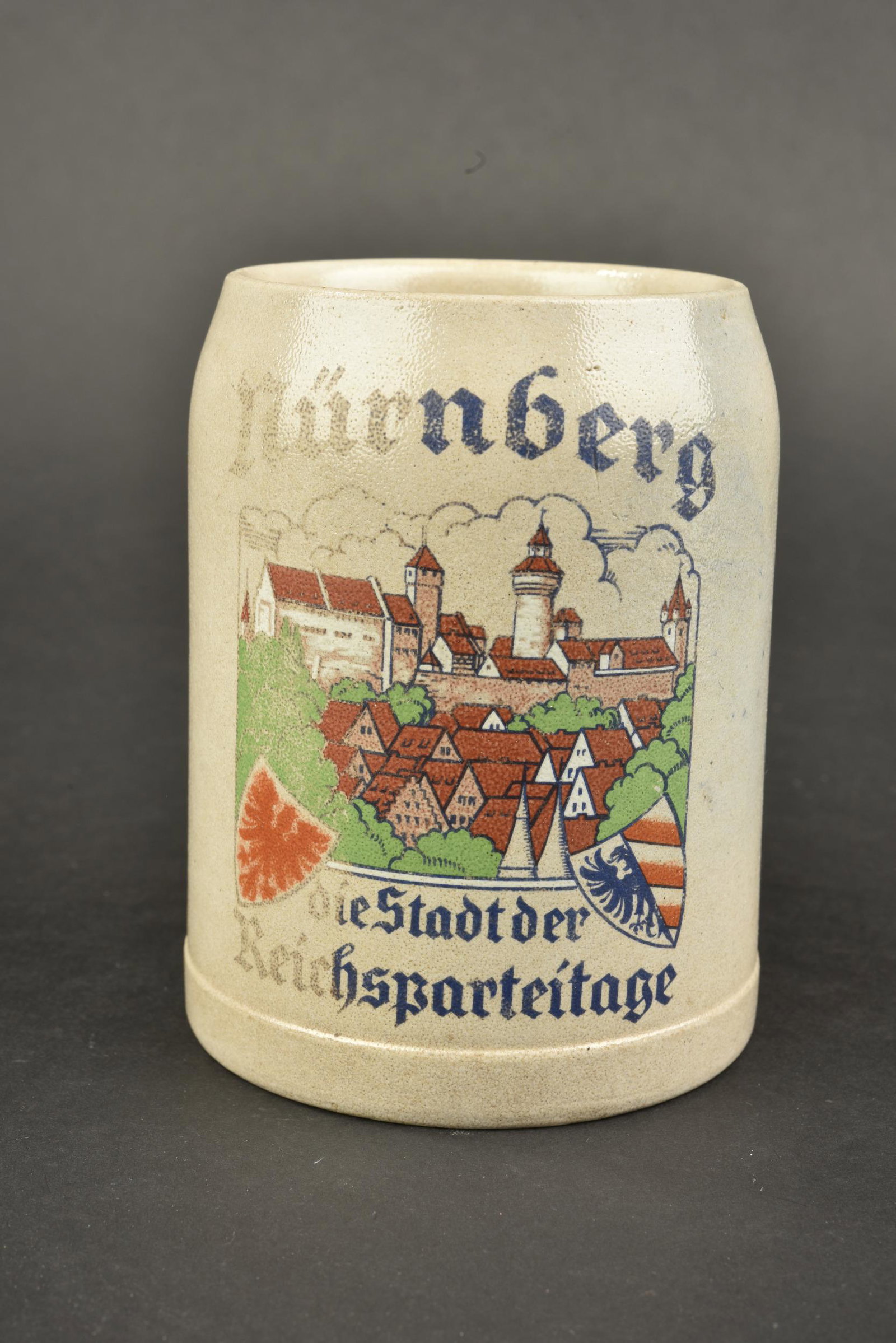 Chope Reichsparteitag. Reichsparteitag mug.: Chope du Reichsparteitag. En gres. Un demi litre. Bien marque Nurnberg Die Stadt der Reichsparteitage. Une partie du decors est partiellement absent. A noter une certaine usure et patine de la piece. 
