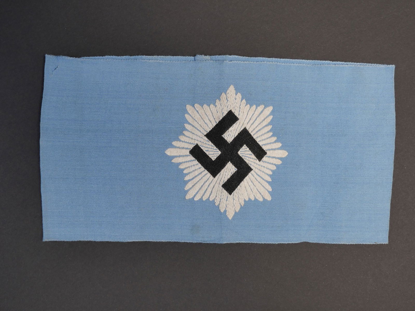Brassard RLB. RLB armband.: Brassard RLB. En tissu coton bleu ciel, insigne du RLB brode. Marquages Bevo Wuppertal. A noter une certaine usure et patine de la piece. Etat I-. RLB armband. Light blue cotton fabric, embroidered RL