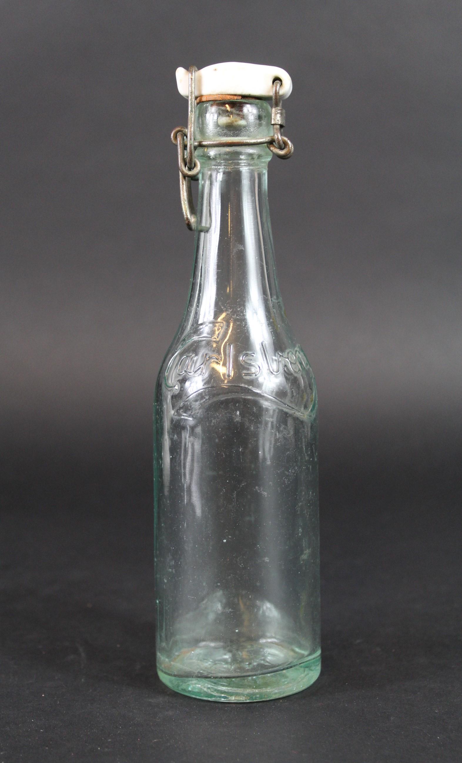 Bouteille Carlsberg. Carlsberg bottle.: Bouteille Carlsberg. En verre blanc. Bouchon en porcelaine blanche. Insigne national present sur le bouchon et au fond de la bouteille. Marquages Carlsberg. A noter une certaine usure et patine de la 