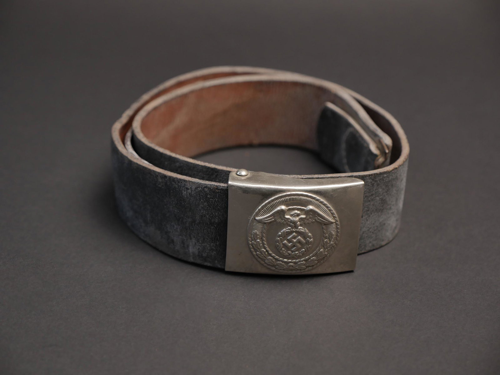 Ceinturon NSKK. NSKK belt.: Ceinturon NSKK. Ceinturon en cuir noir, patte de reglage complete. Bouclerie en metal, tordue et oxydee. Taille 80. Boucle de ceinturon en acier nickele. Sans marquages visibles. A noter une certaine 