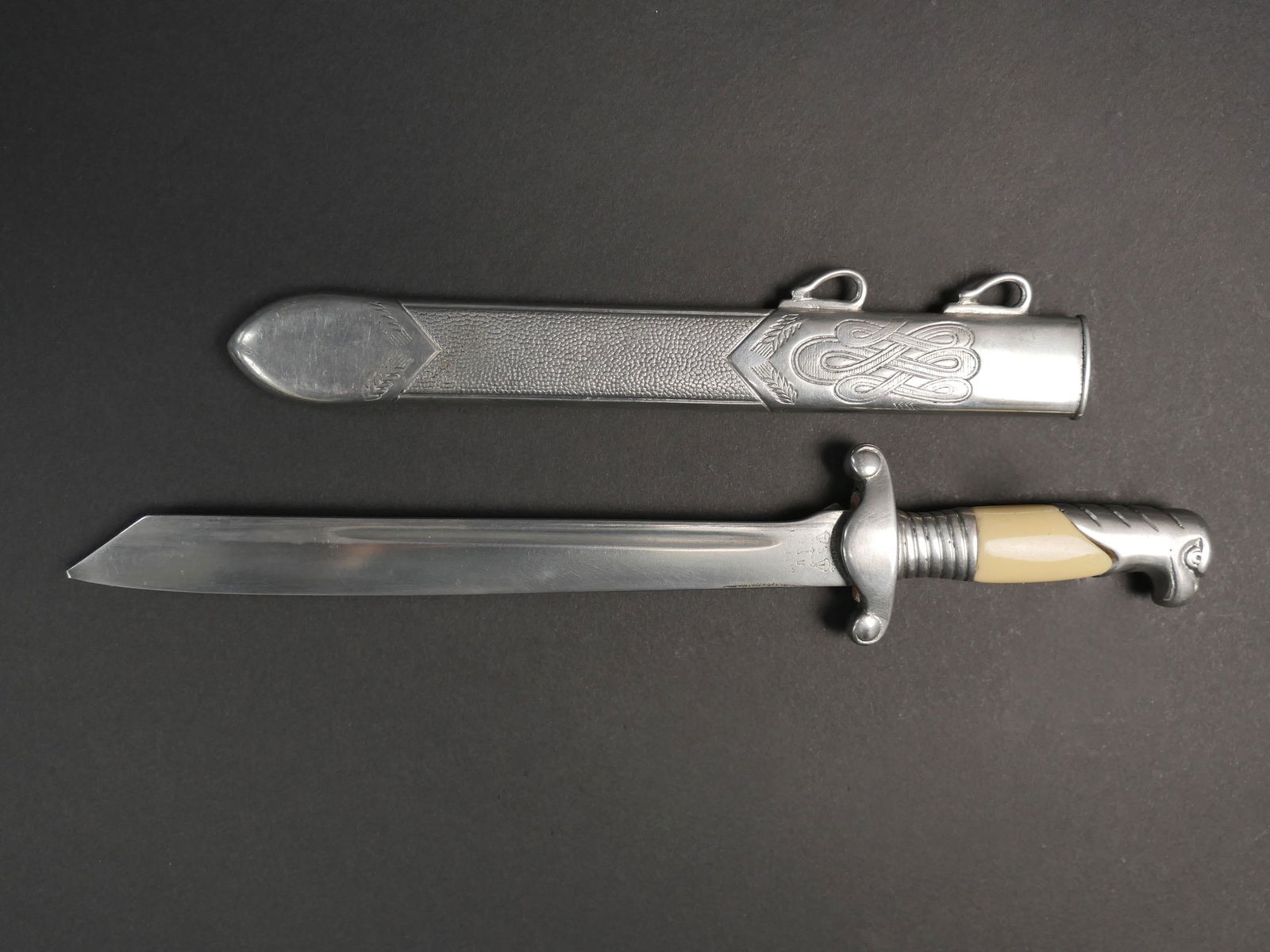 Miniature dague RAD. Miniature RAD dagger.: Miniature de dague RAD. Toutes les garnitures sont en metal couleur argent. Plaquettes imitant l ivoire. Fourreau complet, couleur argent. Belle lame legerement usee. Devise Arbeit Adelt presente. Fab