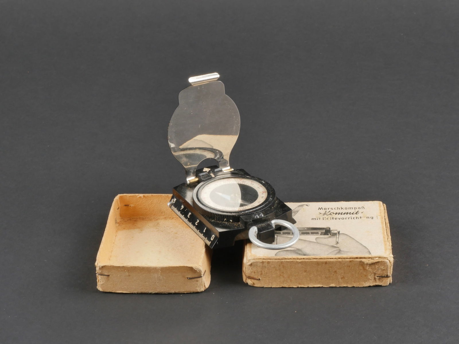 Boussole allemande. German compass.: Boussole allemande. Boite en carton, etiquette collee sur le couvercle. Marquages Marschkompass Kommit mit Halteworrichtung. Contenant une boussole en metal, et bakelite noire. Marquages Kommit German