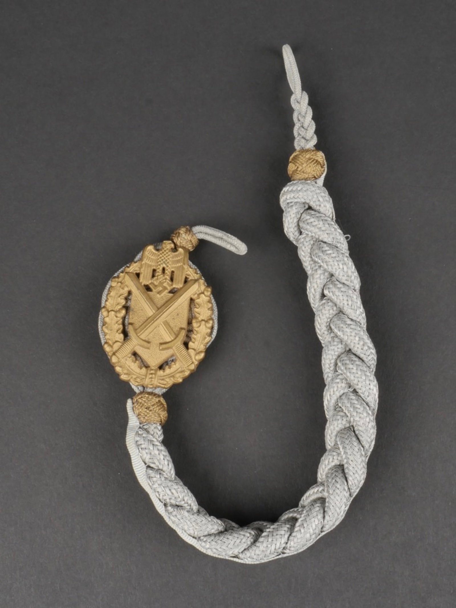 Cordon de tireur Heer. Heer shooter cord.: Cordon de tireur Heer. Tresse en fils argent. Les deux lanieres de fixation sont presentes. . Plaquettes representant un aigle aux ailes repliees et deux epees croisees, et en relief, couleur or. Dos
