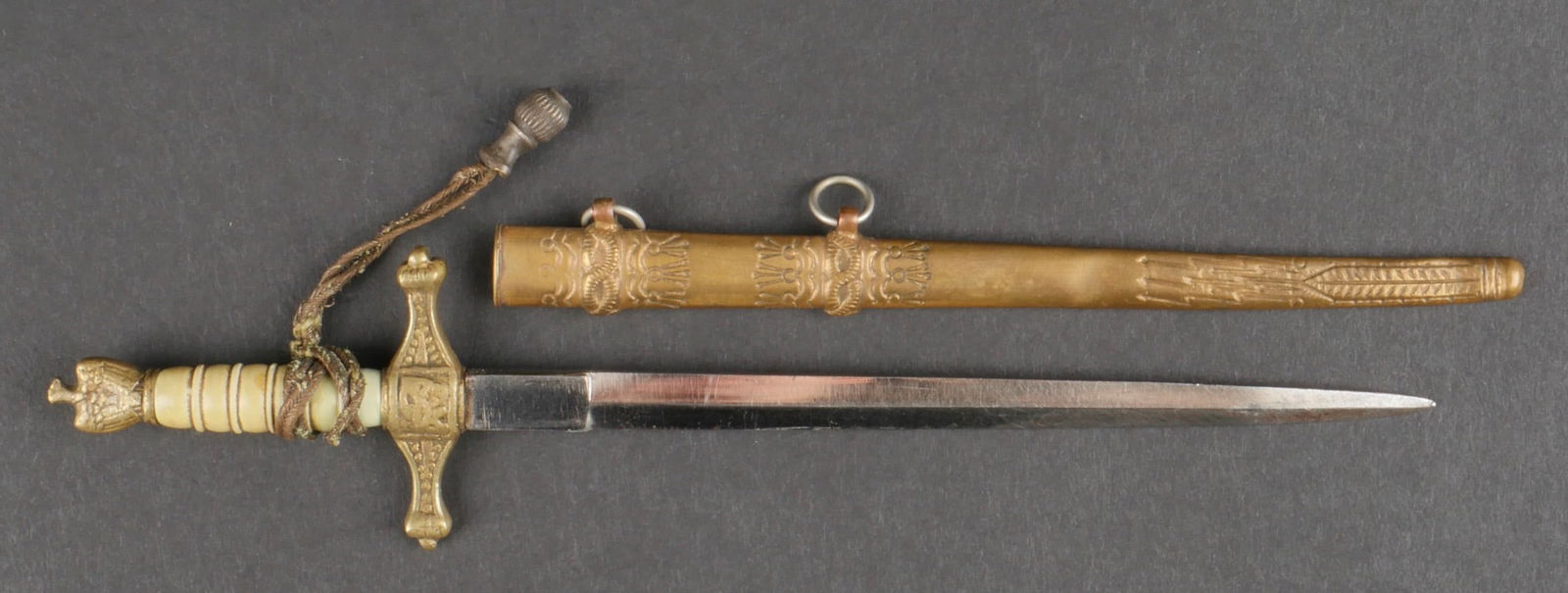Miniature dague KM. Miniature Kriegsmarine dagger.: Miniature de dague de la Kriegsmarine. Garniture en metal, poignee de couleur blanche. Dragonne presente mais tres fragile. Fourreau bossele et partiellement tordu. Belle lame partiellement oxydee. Lo