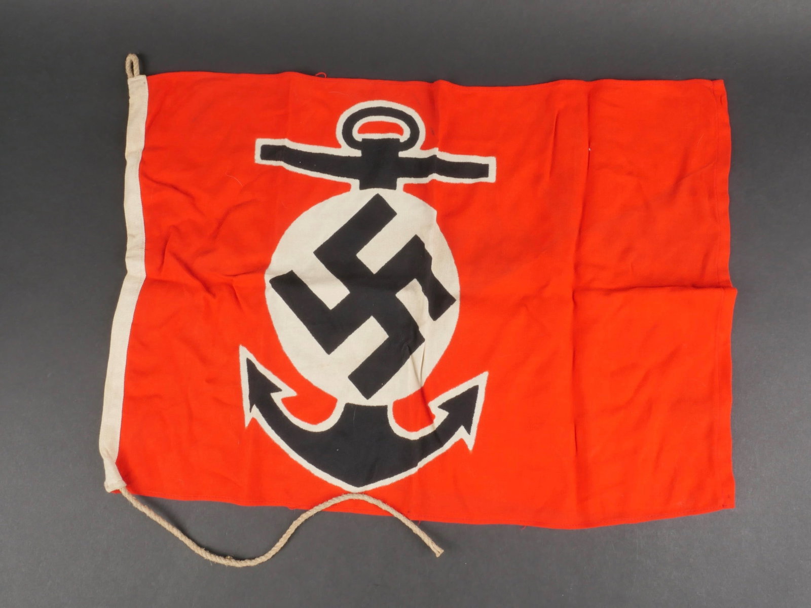 Marque maritime Kriegsmarine. Kriegsmarine maritime mark.: Marque Maritime Kriegsmarine. En tissu coton rouge. Insigne representant une ancre de marine et l'insigne national imprime. Biface. Les cordons de fixation au mat sont presents. Sans marquages visible