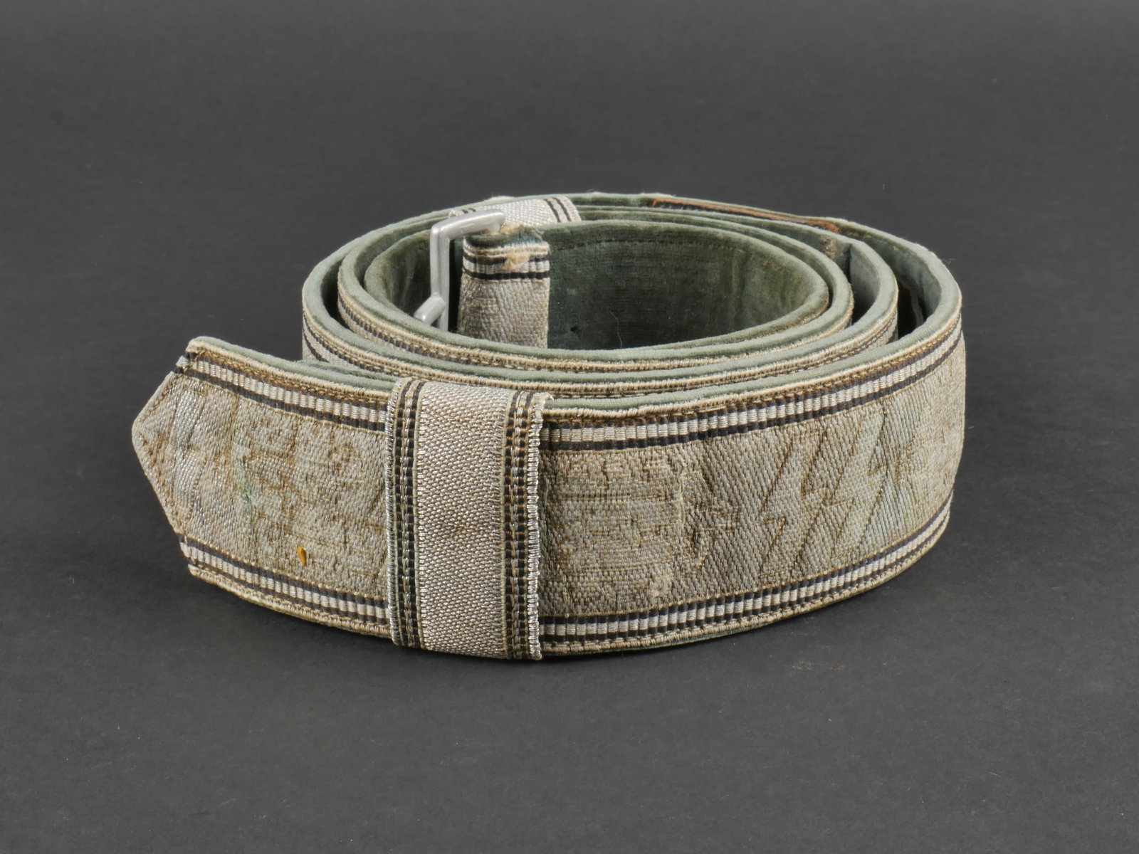 Feldbinde SS. SS Brocade.: Feldbinde d'officier SS. Galon argent decore de runes SS et de feuilles de chene. ceux-ci sont oxydes et passes par le temps. Les deux passants sont presents. Bouclerie en aluminium. Boucle manquante.