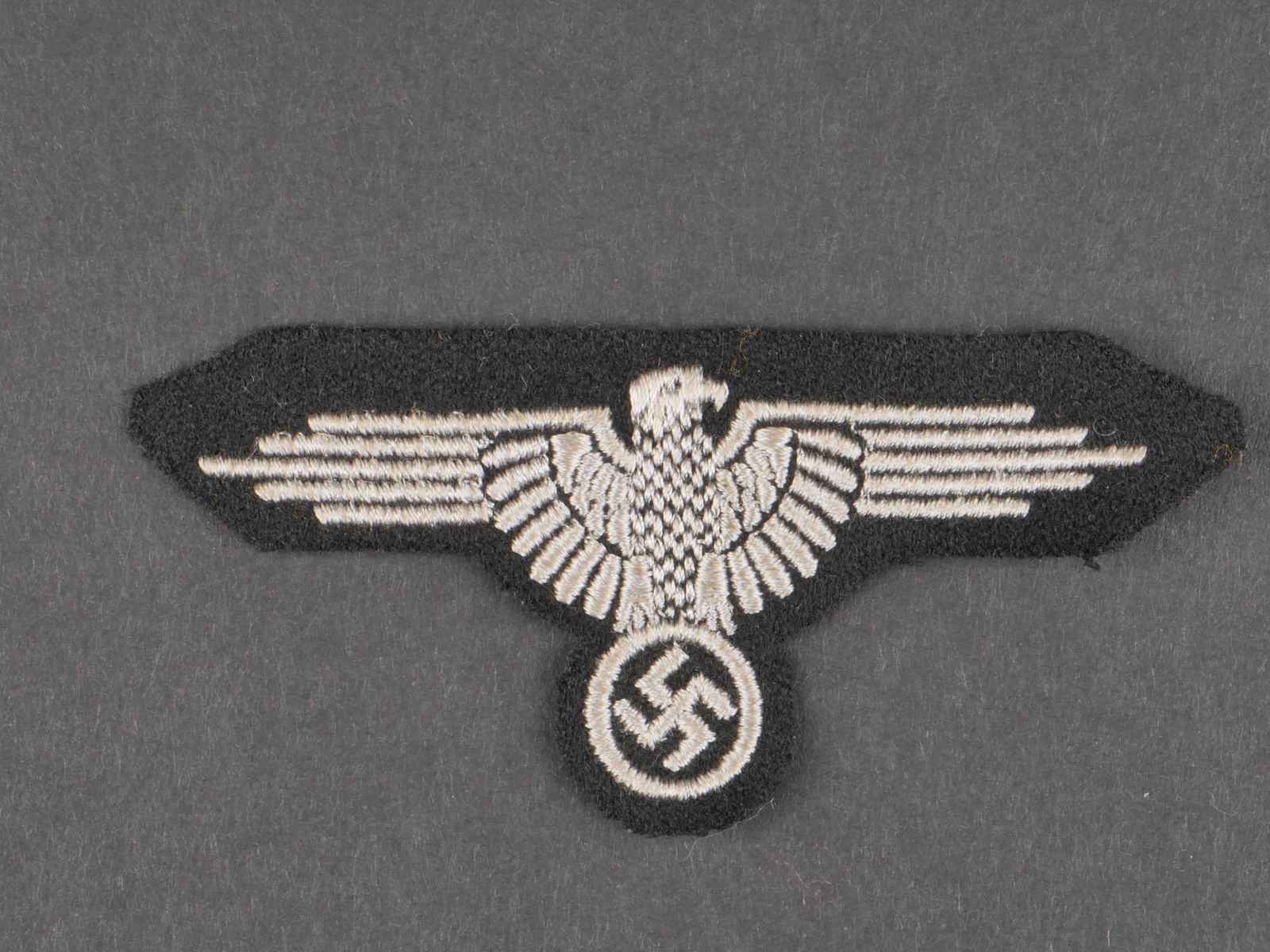 Aigle de bras SS. SS arm eagle.: Aigle de bras SS. Modele Dachau, brode sur fond noir, jamais monte. A noter une legere patine de la piece. Etat I-. SS arm eagle. Dachau model, embroidered on black background, never mounted. Note sli