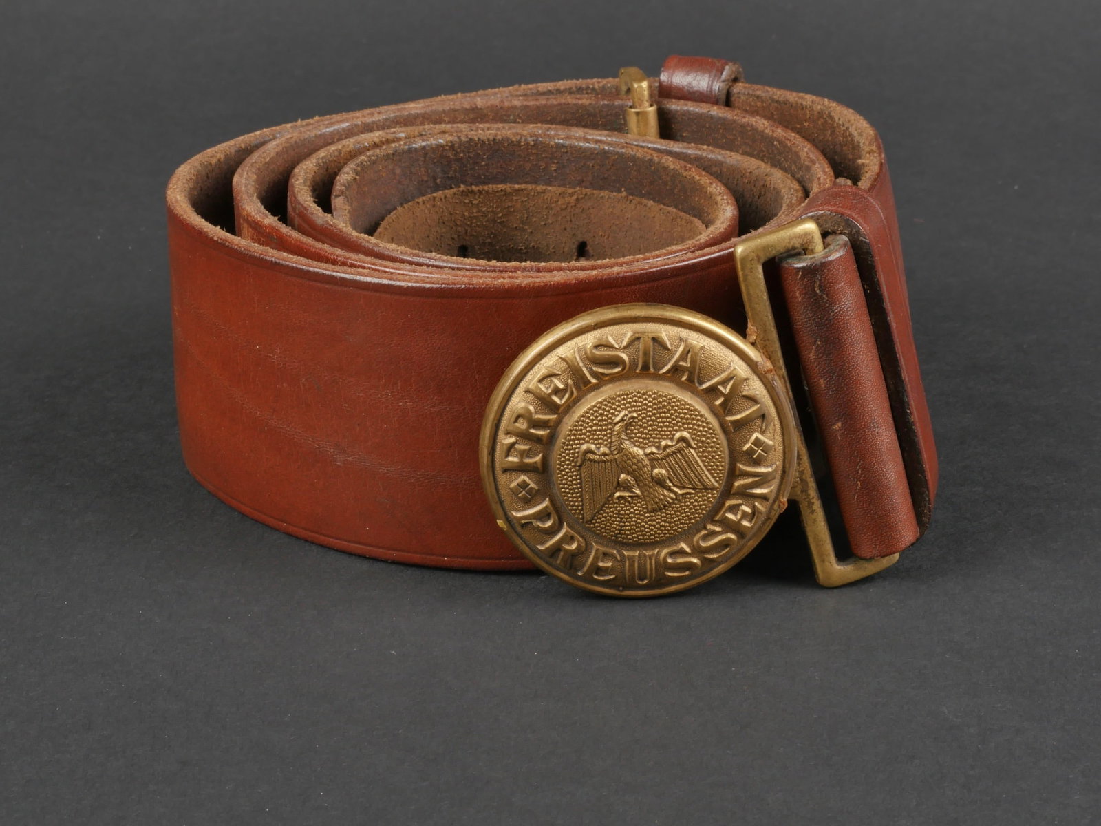 ceinturon Freistaat Preussen. Freistaat Preussen belt.: ceinturon Freistaat Preussen. ceinturon en cuir marron, les passants en cuir sont presents. Fabrication FW Assmann Ludenscheid. Date 1942. Bouclerie complete. La patte de reglage en cuir est complete.