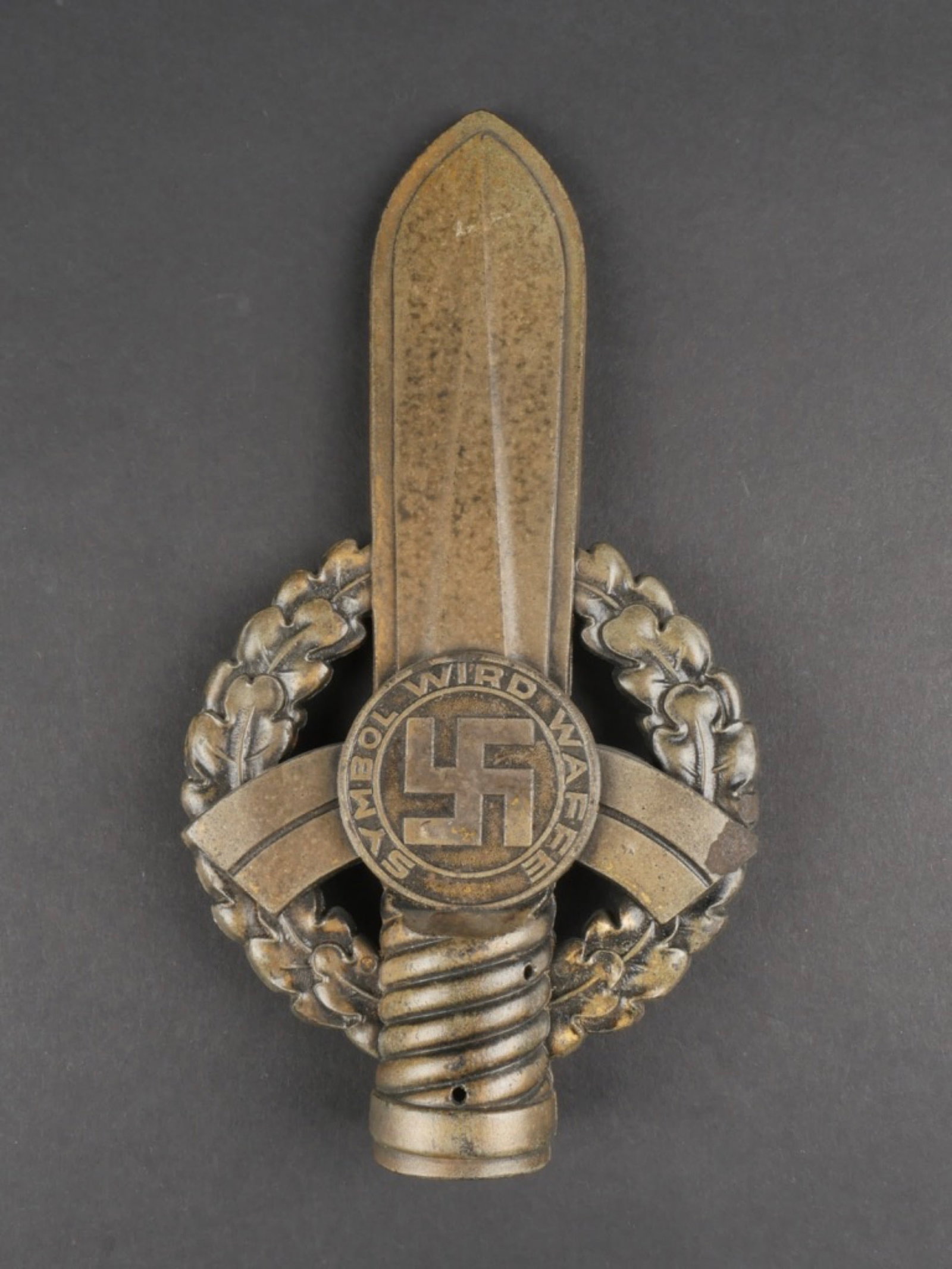 Pointe de drapeau NS Reichskriegerbundes. NS Reichskriegerbundes flag tip.: Pointe de drapeau NS Reichskriegerbundes. En matiere plastique, patine couleur bronze a 80%. Bien marque Symbol wird Waffen 1940. Beau design d'une croix de fer de premiere classe au dos de la piece. 