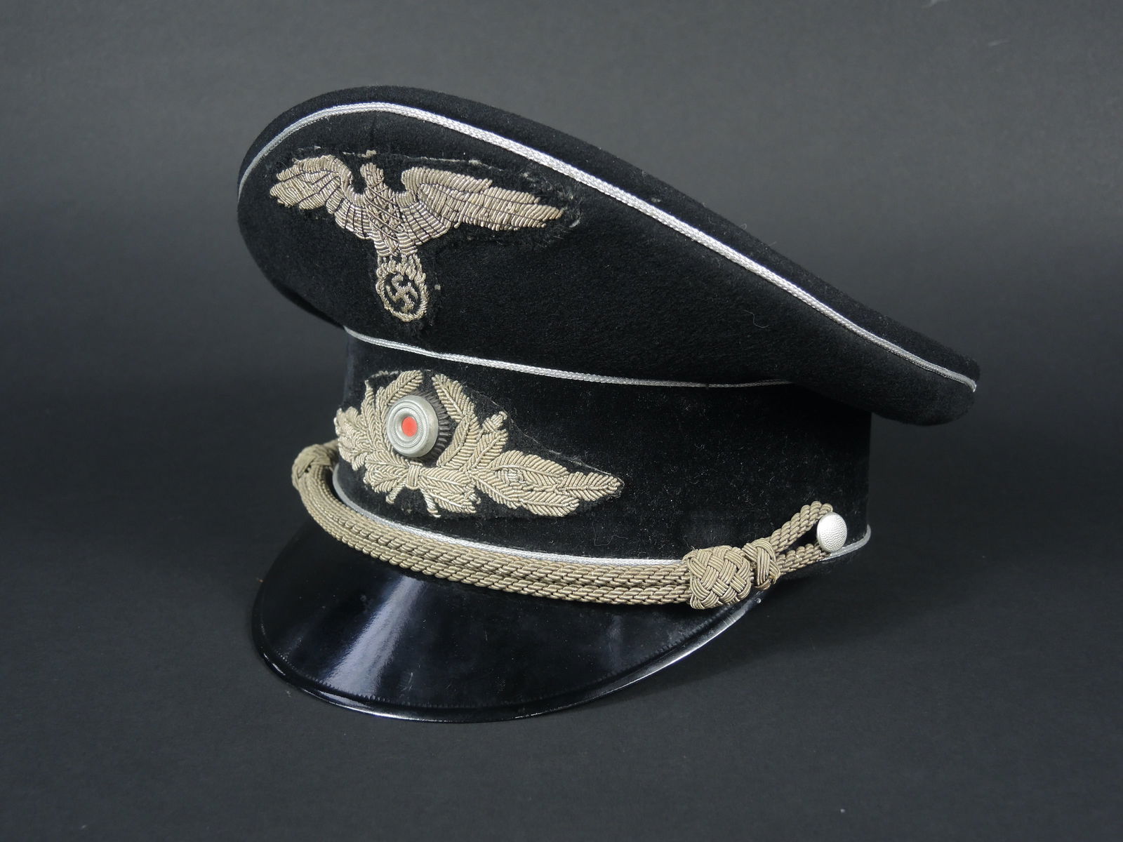 casquette de diplomate. Graduate cap.: casquette de diplomate allemand. Fabrication dit des territoires occupes. En drap noir. Triple lisere argente faisant le tour de la coiffe. Fausse julaire complete. Aigle et feuilles de chene en canne