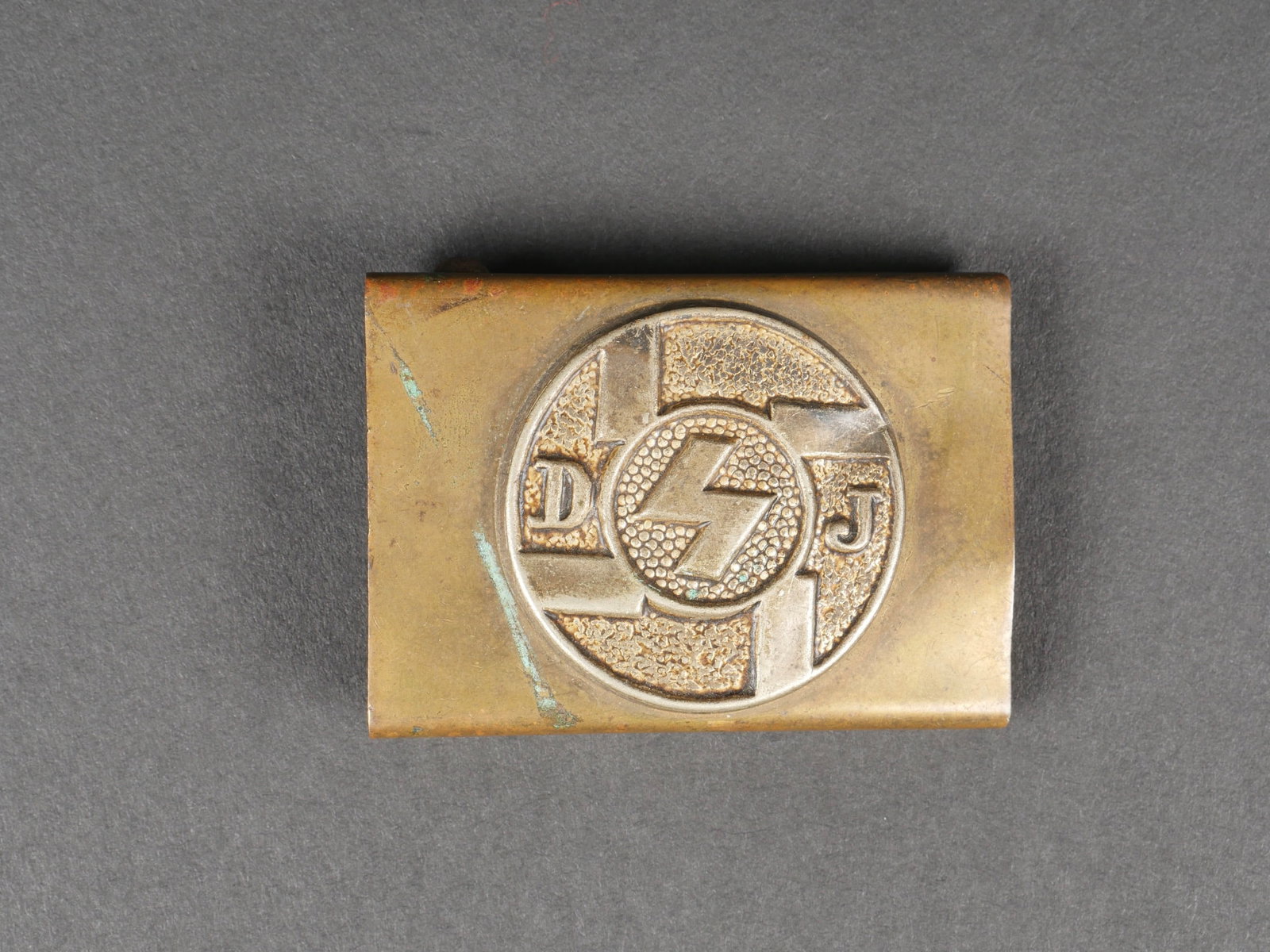 Boucle de ceinturon DJ. Deutsche jungvolk belt buckle.: Boucle de ceinturon Deutsche Junksvolks. En laiton, fabrication en deux parties. Marquage DJ en relief. Boucle a deux ardillons presente. Les soudures au dos semblent avoir ete refaites. Sans marquage