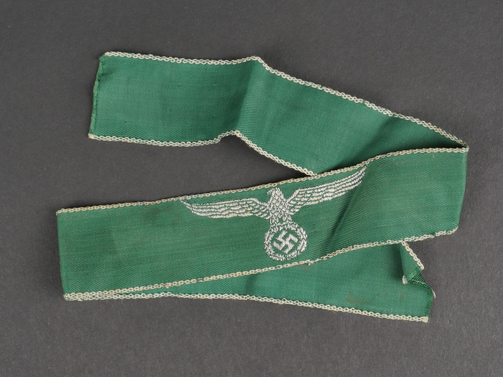 Bande de bras douane. German custom sleeve band.: Bande de bras des douanes. En tissu tisse vert. Aigle des douanes tisse en fil argente. Longueur 44 cm. A noter une certaine usure et patine de la piece, ainsi que quelques taches et traces de colle.