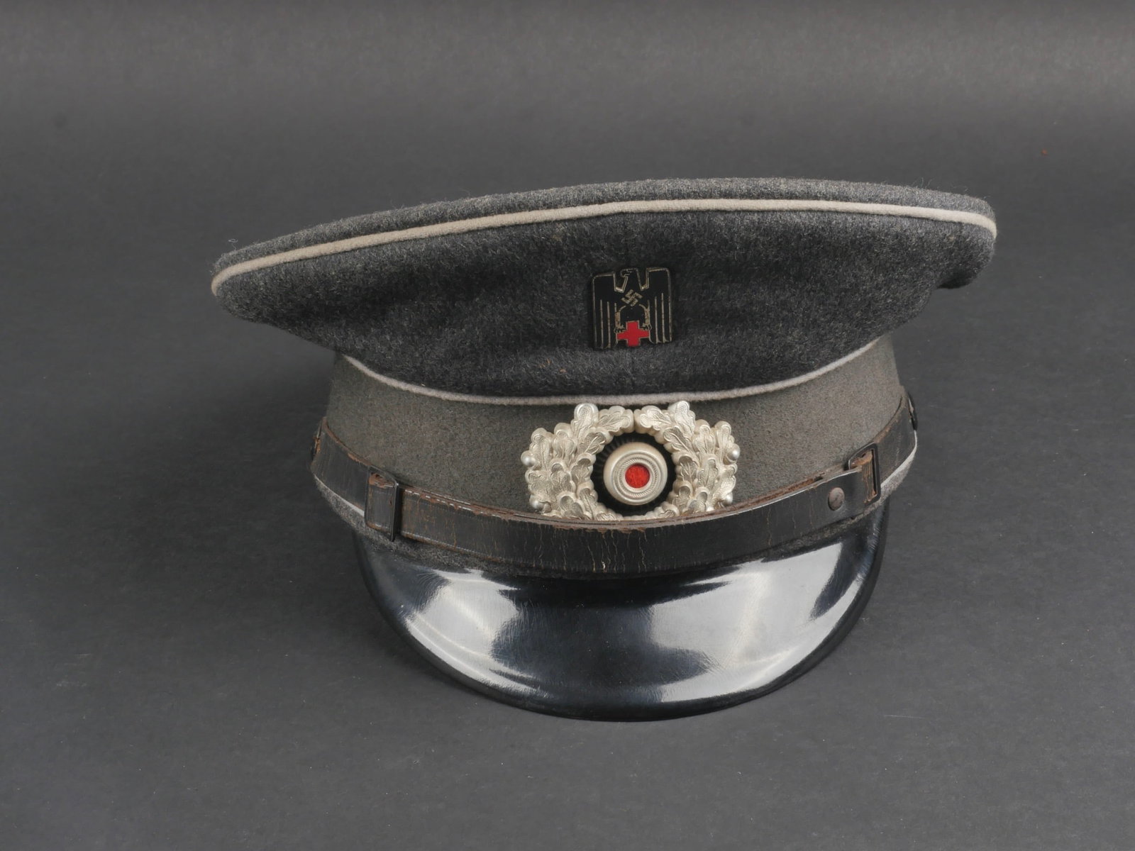 casquette DRK. German DRK cap.: casquette DRK. En drap gris. Bandeau en drap gris clair. Triple lisere gris clair. Insignes metalliques. Les insignes n'ont pas ete demontes afin de verifier les attaches. Jugulaire en cuir complete. 