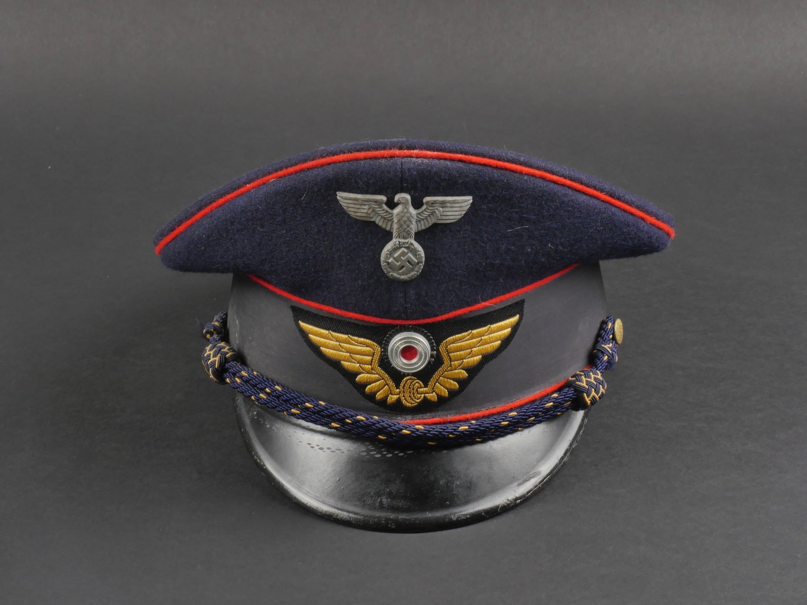 casquette Reichsbahn. German Reichsbahn cap.: casquette Reichsbahn. En drap bleu marin. Triple lisere rouge. Aigle et cocarde metallique. Les insignes n'ont pas ete demontes afin de verifier les attaches. Bandeau en tissu noir. Feuilles de chene 