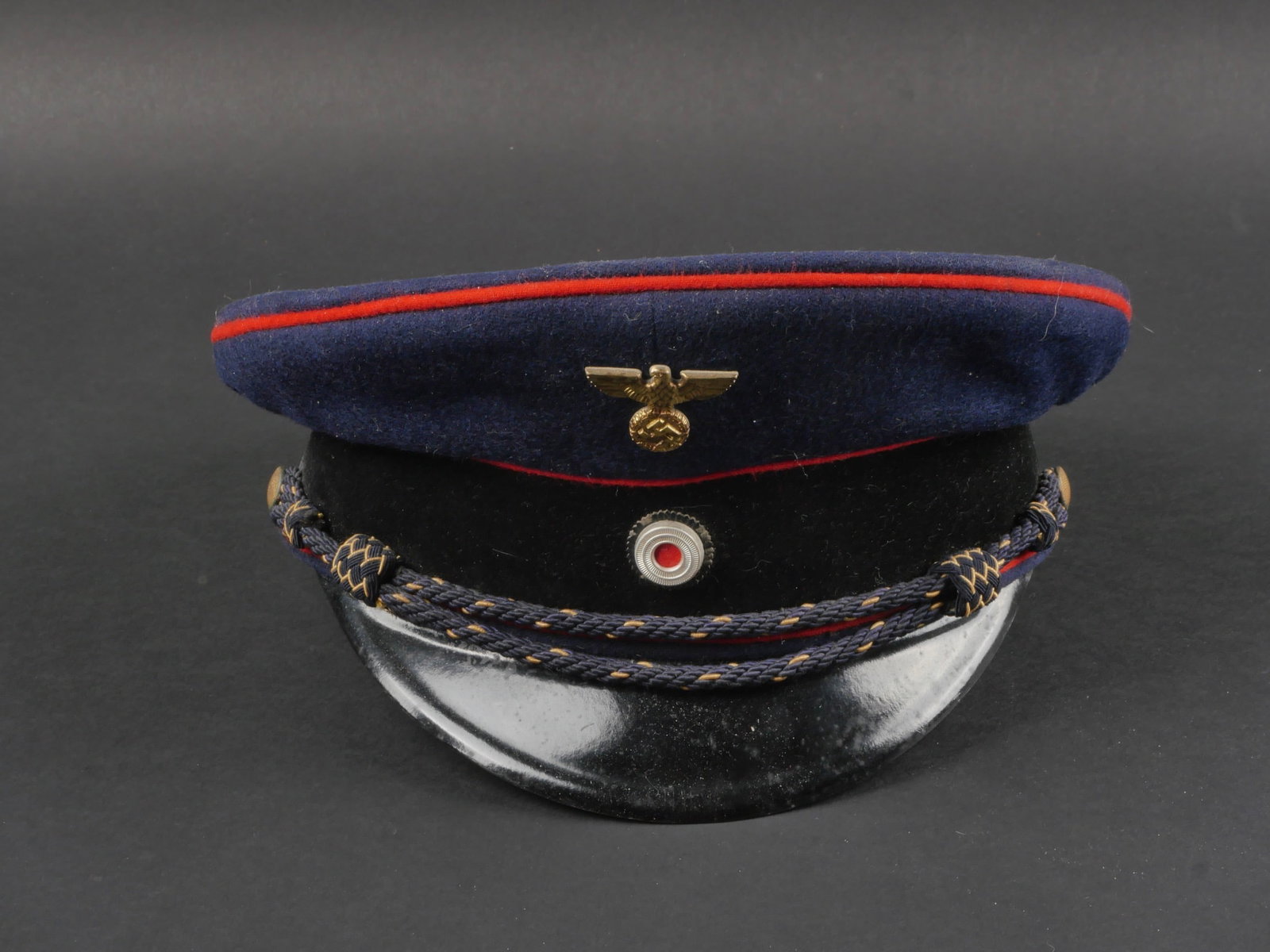 casquette Reichsbahn. German Reichsbahn cap.: casquette Reichsbahn. En drap bleu marin. Triple lisere rouge. Aigle et cocarde metallique. Les insignes n'ont pas ete demontes afin de verifier les attaches. Bandeau en tissu noir. Feuilles de chene 