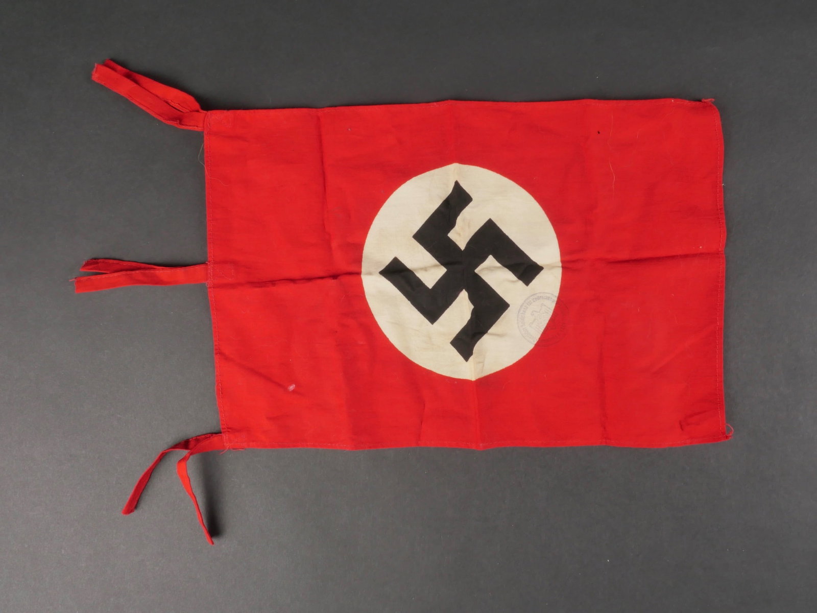 Drapeau allemand. German flag.: Drapeau allemand. En tissu coton rouge. Insigne national rapporte. Biface. Trois cordons de fixation au mat. Tampon du Reichsportbund partiellement illisible. Dimensions 22 x 24 cm. A noter une certai