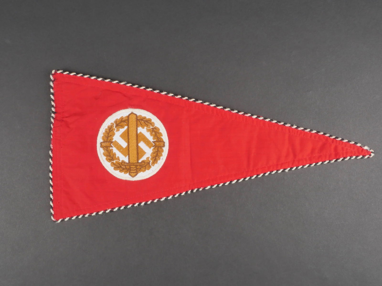 Fanion des sports SA. German SA Sport pennant.: Fanion des sports de la SA. En tissu coton rouge, borde d'un lisere noir et blanc. Insigne des sports de la SA tisse et rapporte. Biface. Le systeme de fixation est manquant. Dimensions 18 x 38,5 cm.