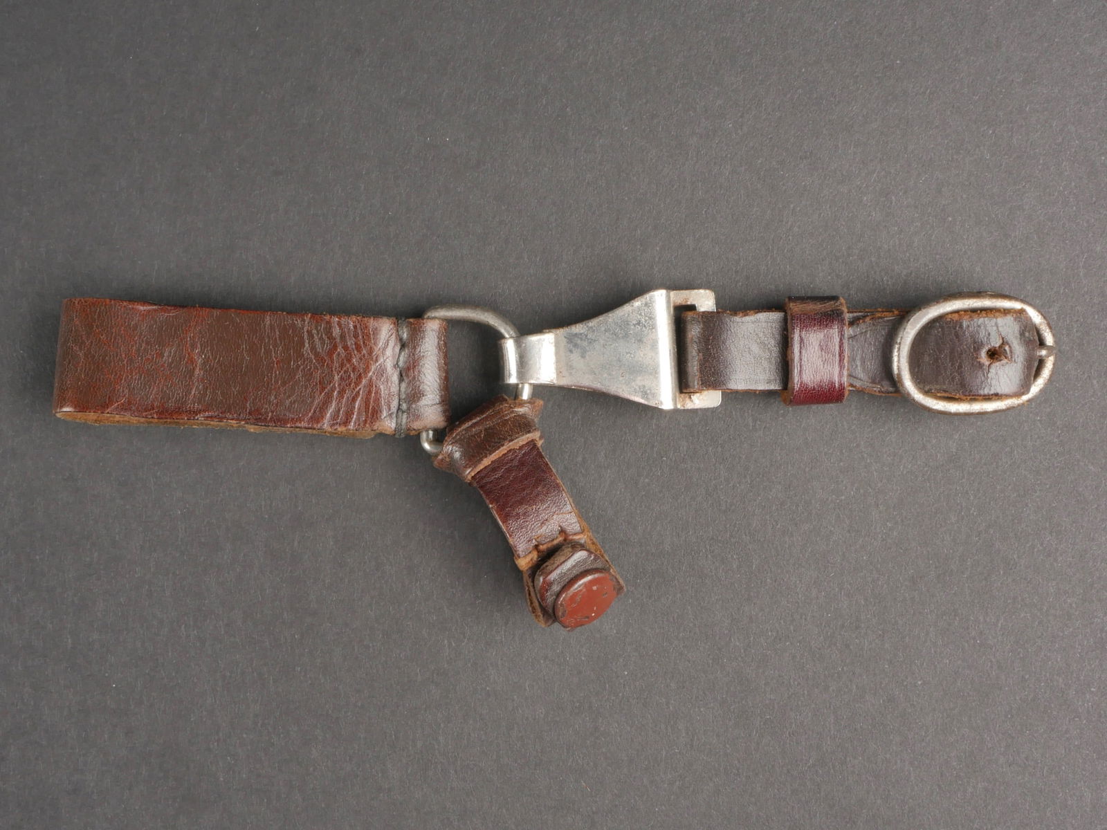 Attache dague SA. SA dagger clip.: Attache pour dague SA/NSKK. En cuir marron. Le passant au ceinturon est complet avec son anneau metallique. L'attache a la poignee est complete avec son bouton pression fonctionnel. Attache de dague e