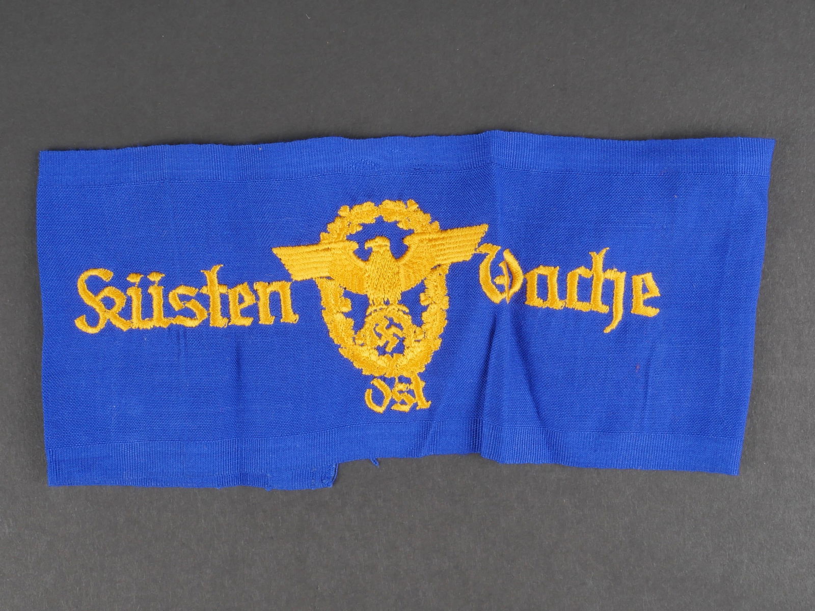 Brassard Kusten Wache Ost. Kusten Wache Ost armband.: Brassard Kusten Wache Ost. En tissu coton bleu roi. Insigne et mention Kusten Wache ost, brodes en fil jaune or. La couture arriere est defaite. A noter une certaine usure et patine de la piece. Etat
