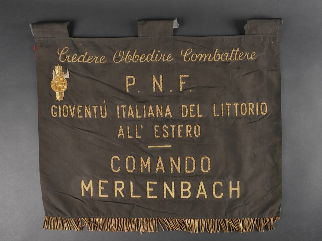 Fanion du commandement de la section fasciste de la Jeunesse Italienne du Licteur a l’etranger de: Fanion du commandement de la section fasciste de la Jeunesse Italienne du Licteur a l’etranger de la ville de Merlenbach en Moselle. En tissu soyeux biface, une face noir brodee de cannetille or et 