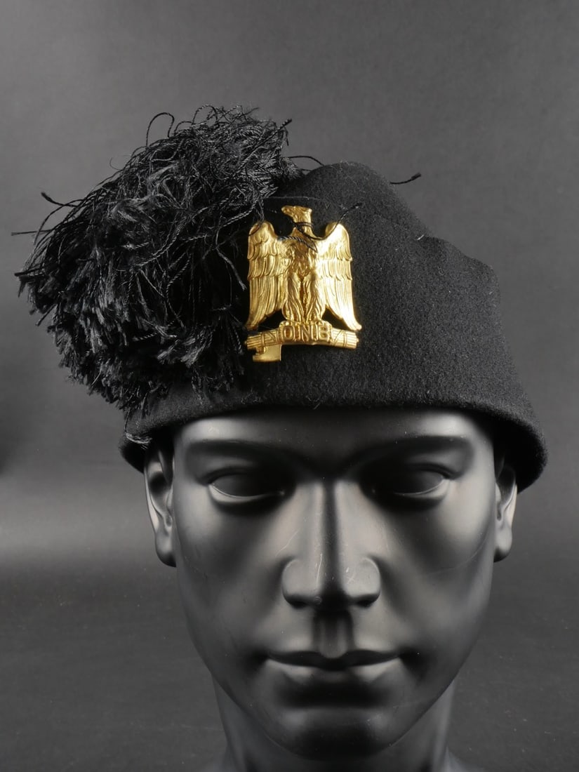 Coiffure de mouvement de jeunesse fasciste. Fascist youth movement headdress.: Coiffure de mouvement de jeunesse fasciste. Comprenant un fez en feutre des Opera Nationale Ballilas, complet avec son pompon et son insigne metallique dore. Etat II-. Fascist youth movement headdress