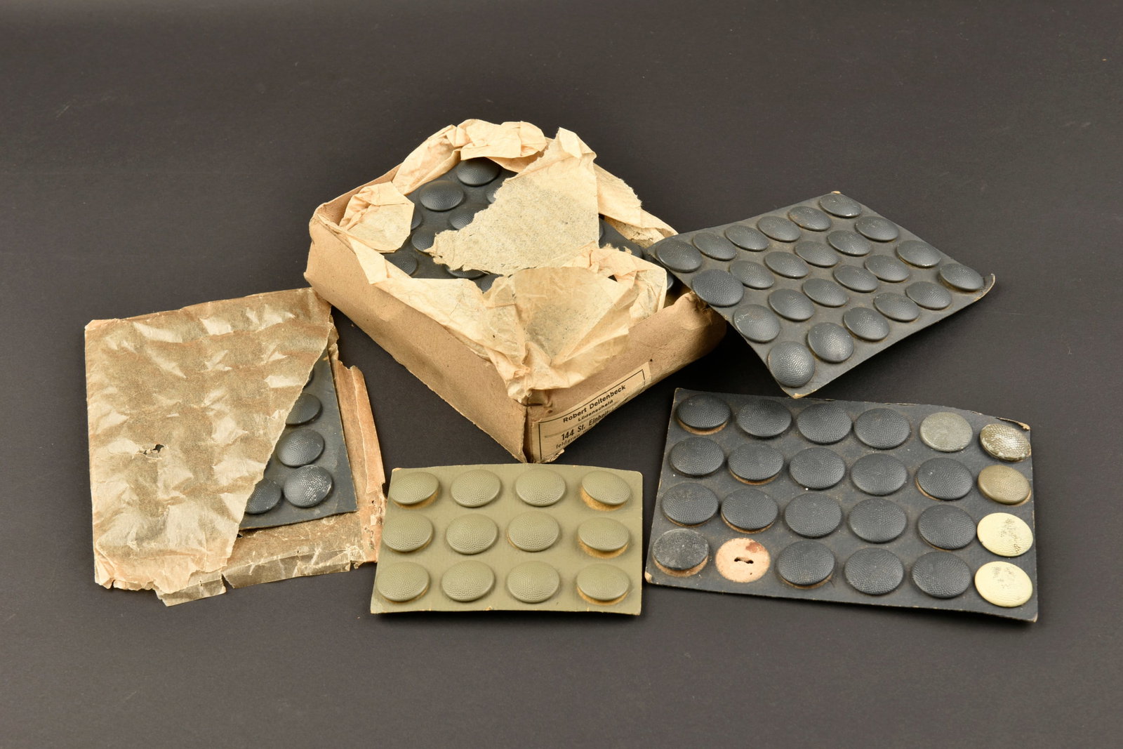 Boutons allemand. German buttons.: Boutons allemand. Comprenant 138 boutons greneles bleu fonces. Deux boutons greneles blanc. 15 Boutons en metal grenele Feldgrau. Sur carton complet, certains papier d emballage sont presents. A noter