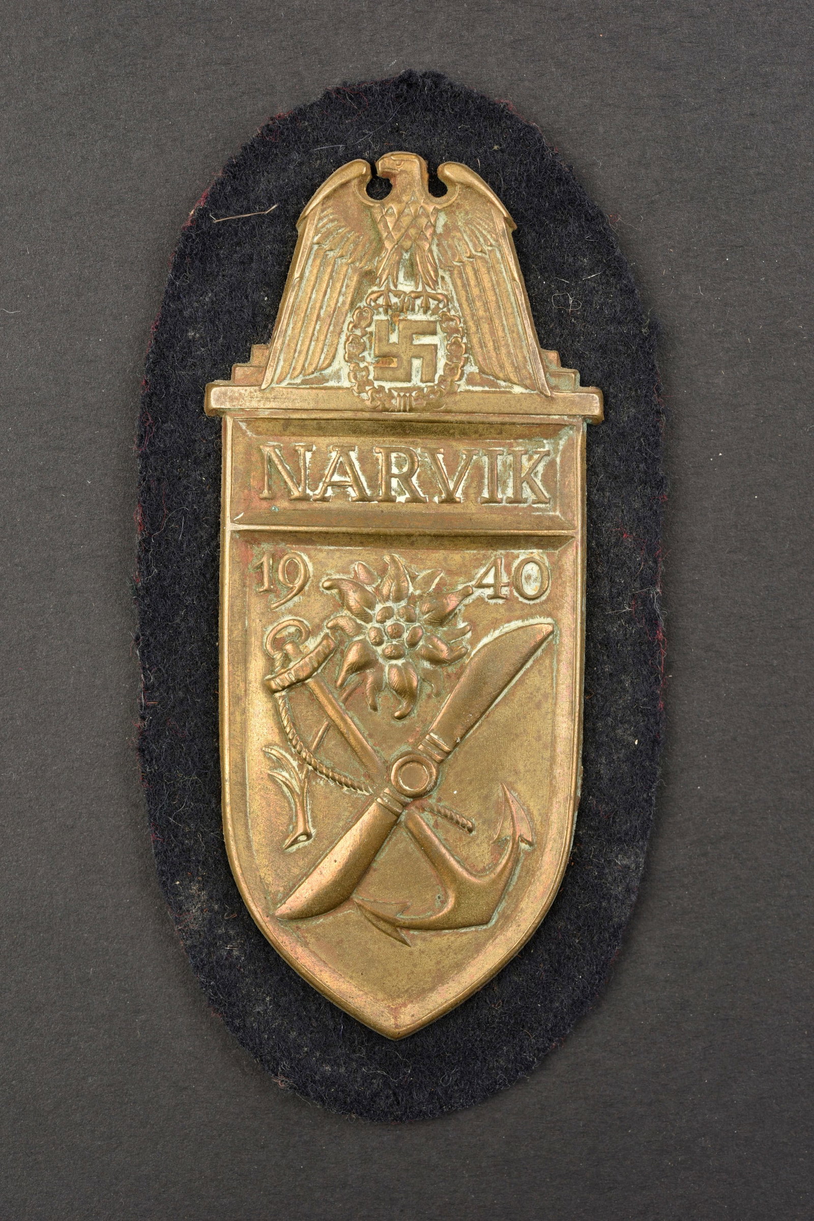 Narvikschild.: Plaque commemorative Narvik. Plaque en metal embouti, monte sur fond en drap bleu marine type Kriegsmarine. Dos de la piece double de papier noir. Fabrication Deumer. A noter une certaine usure et pat