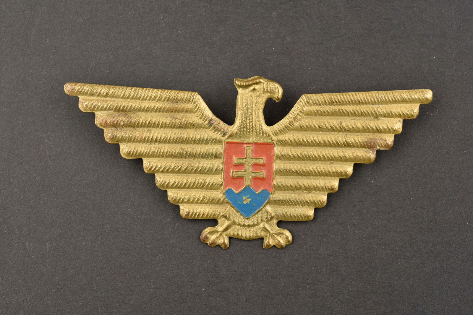 Aigle de coiffure slovaque. Slovak headdress eagle.: Aigle de coiffure Slovaque. En metal dore, ecu disposant des arme de la Slovaquie. Les attaches au dos sont presente. A noter une certaine usure et patine de la piece. Etat II+. Slovakian headdress ea