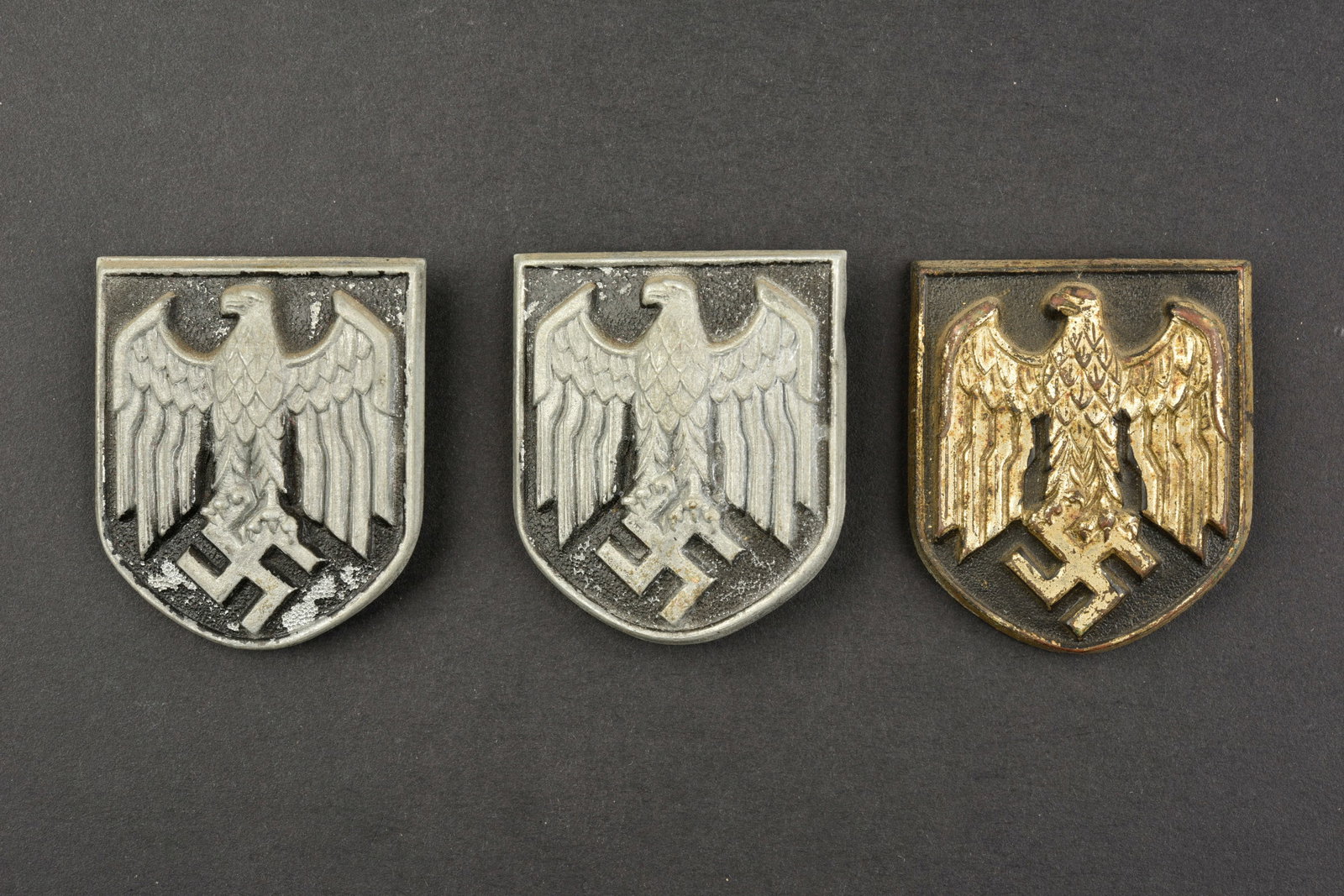 Insignes de casque tropical. Tropical helmet badges.: Insignes de casque tropical. Deux modeles d aigle pour casque tropicaux de la Heer, les attaches sont presentes. Un modele d aigle pour casque tropical de la Kriegsmarine, dorure tres abimee, les patt