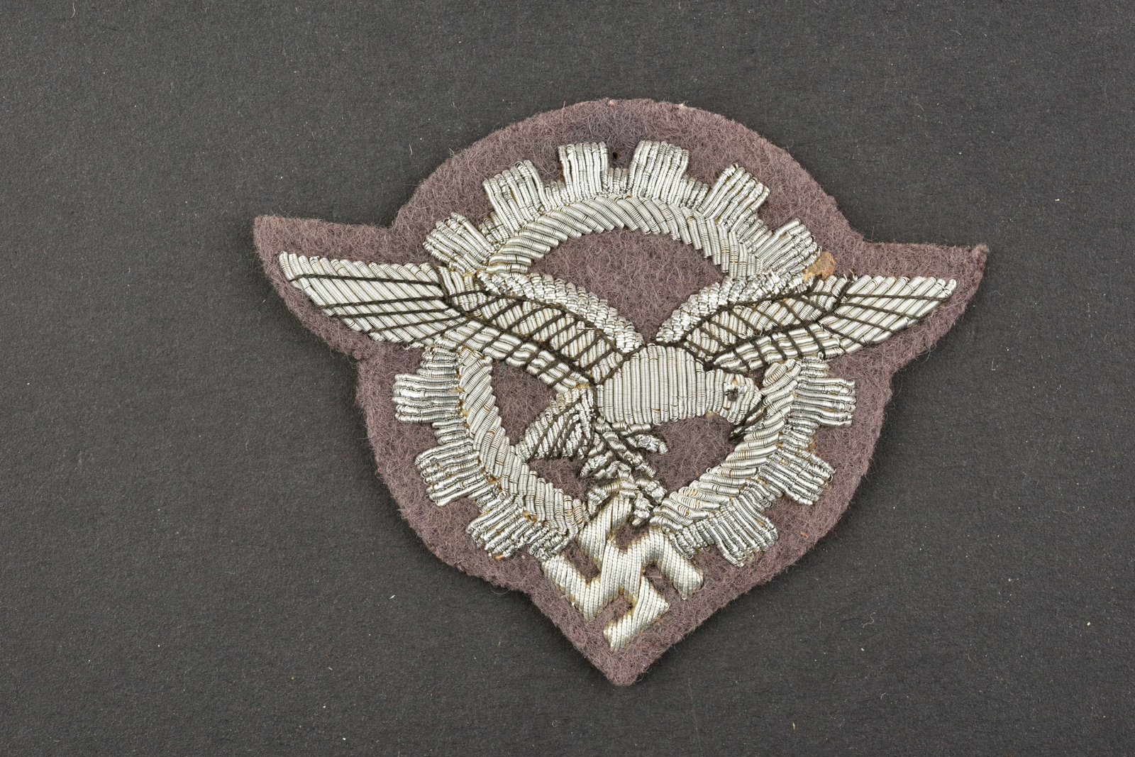 Insigne d ingenieur LW. LW engineer s badge.: Insigne de coiffure d ingenieur de la Luftwaffe. Modele pour officier en cannetille argent, sur fond en drap violet. Dos de la piece double de papier noir. A noter une certaine usure et patine de la p