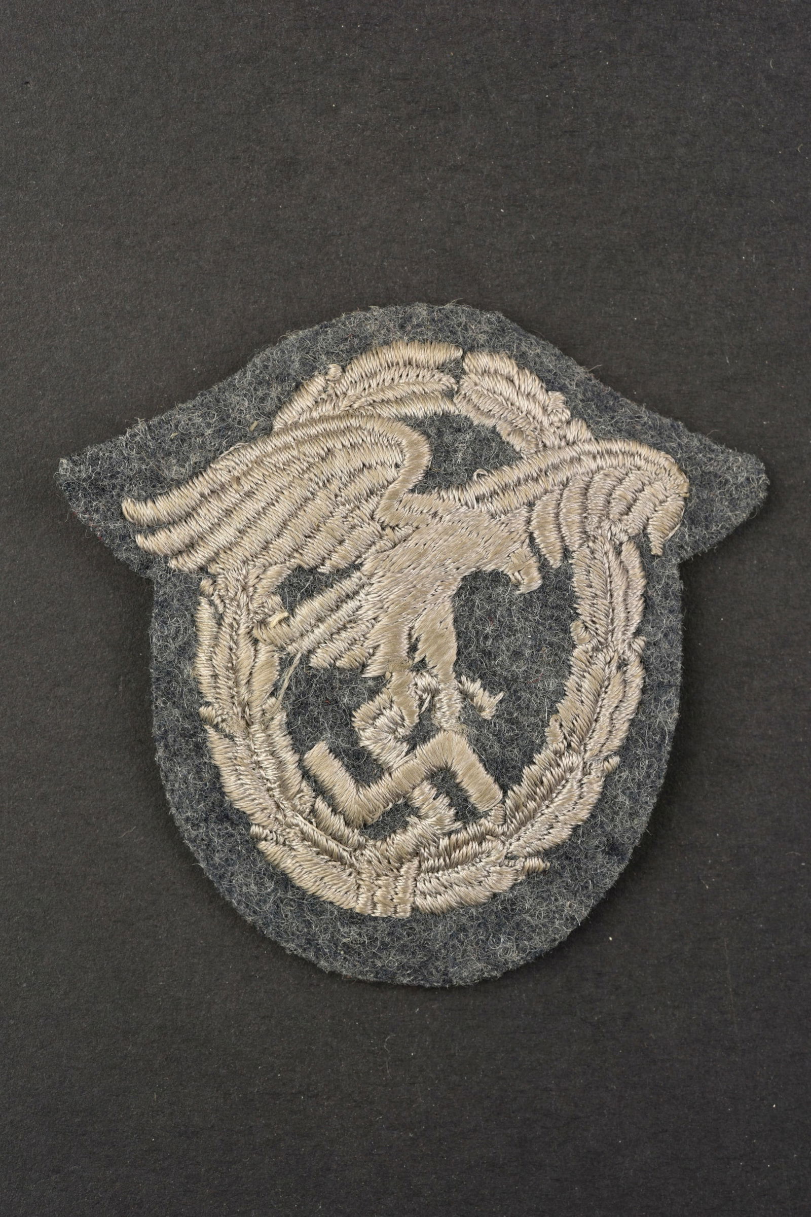 Beobachterabzeichen.: Beobachterabzeichen. Fabrication bombee. Brodee sur fond en drap gris/bleu. Dos de la piece double en tissu noir. A noter une certaine usure et patine de la piece, ainsi que des traces de colle au dos